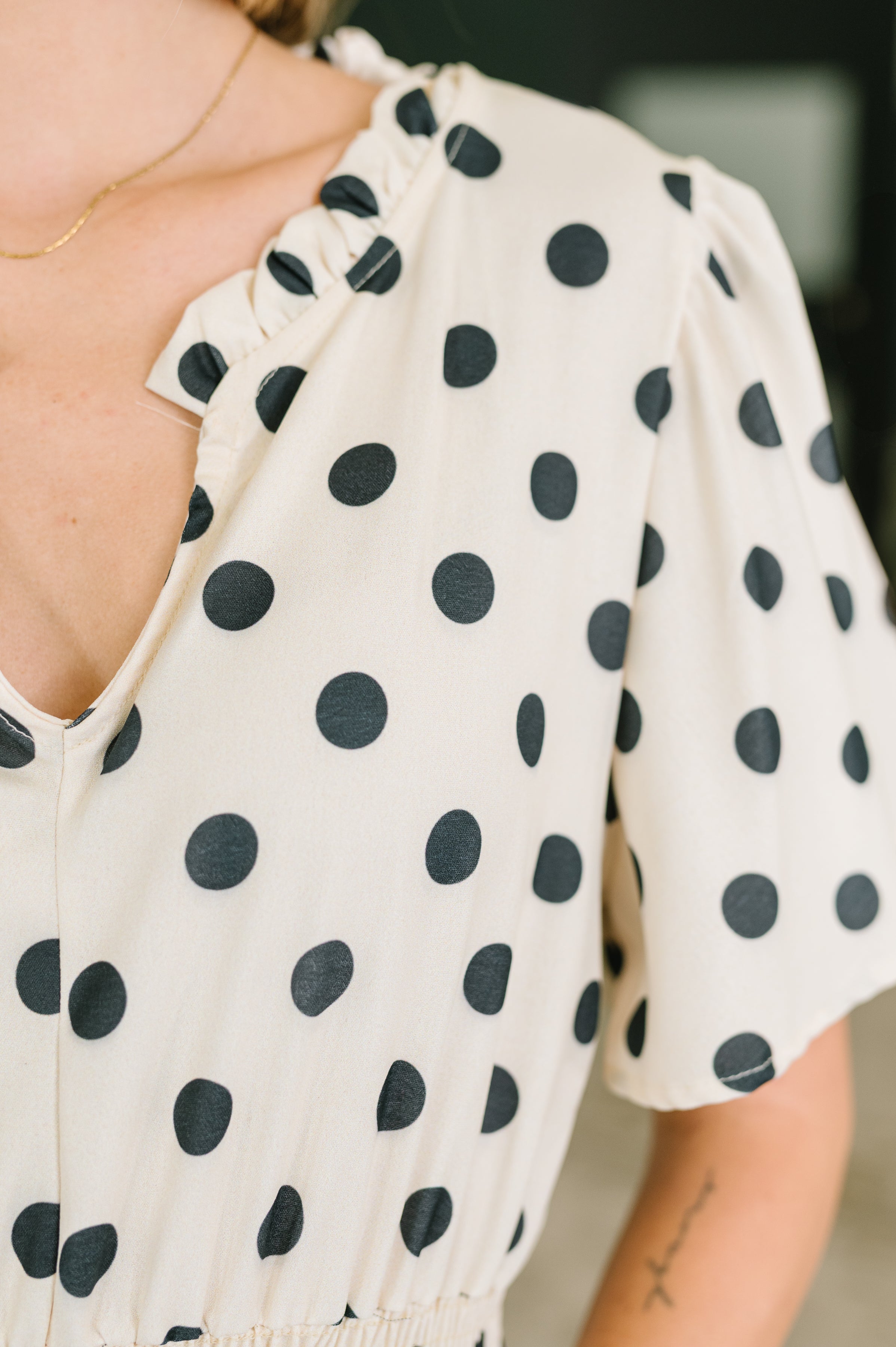 Close-up of ivory midi dress with black polka dots, ruffled V-neckline, and gathered bell sleeves on model indoors