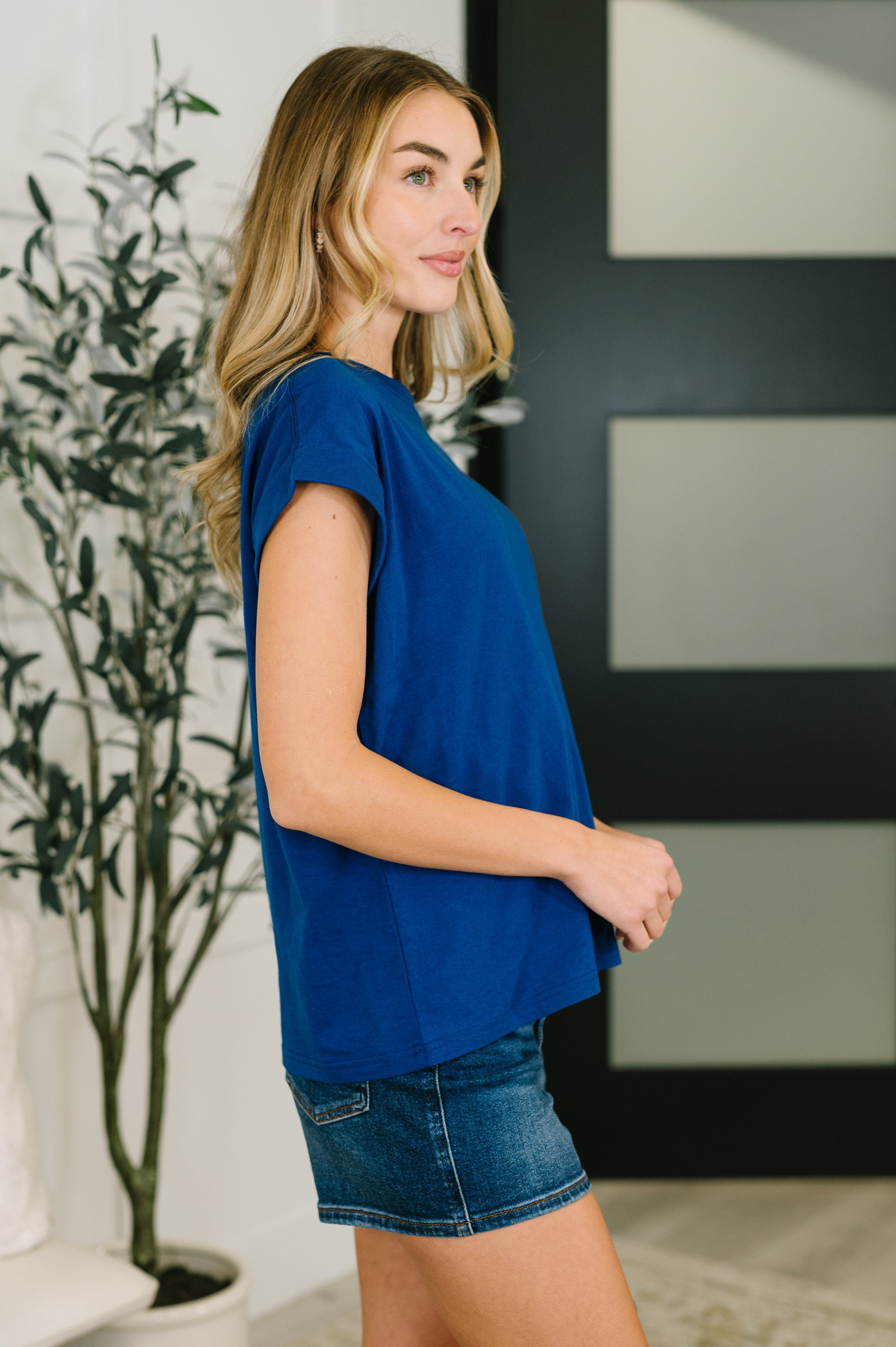 Woman wearing blue basic rolled sleeve t-shirt paired with denim skirt standing indoors in profile view