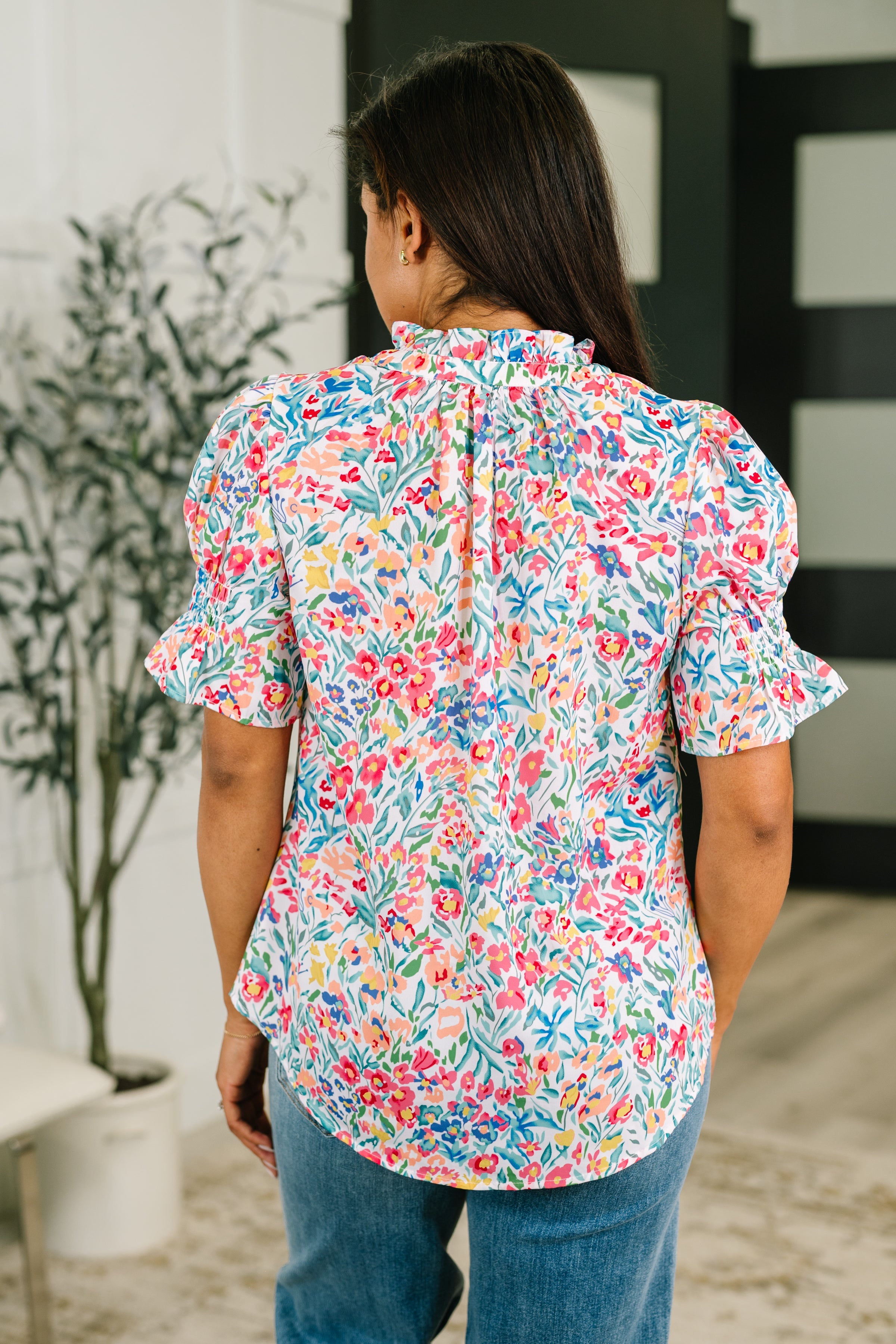 Woman wearing a colorful floral blouse with ruffled sleeves and neckline in a bright eclectic indoor setting