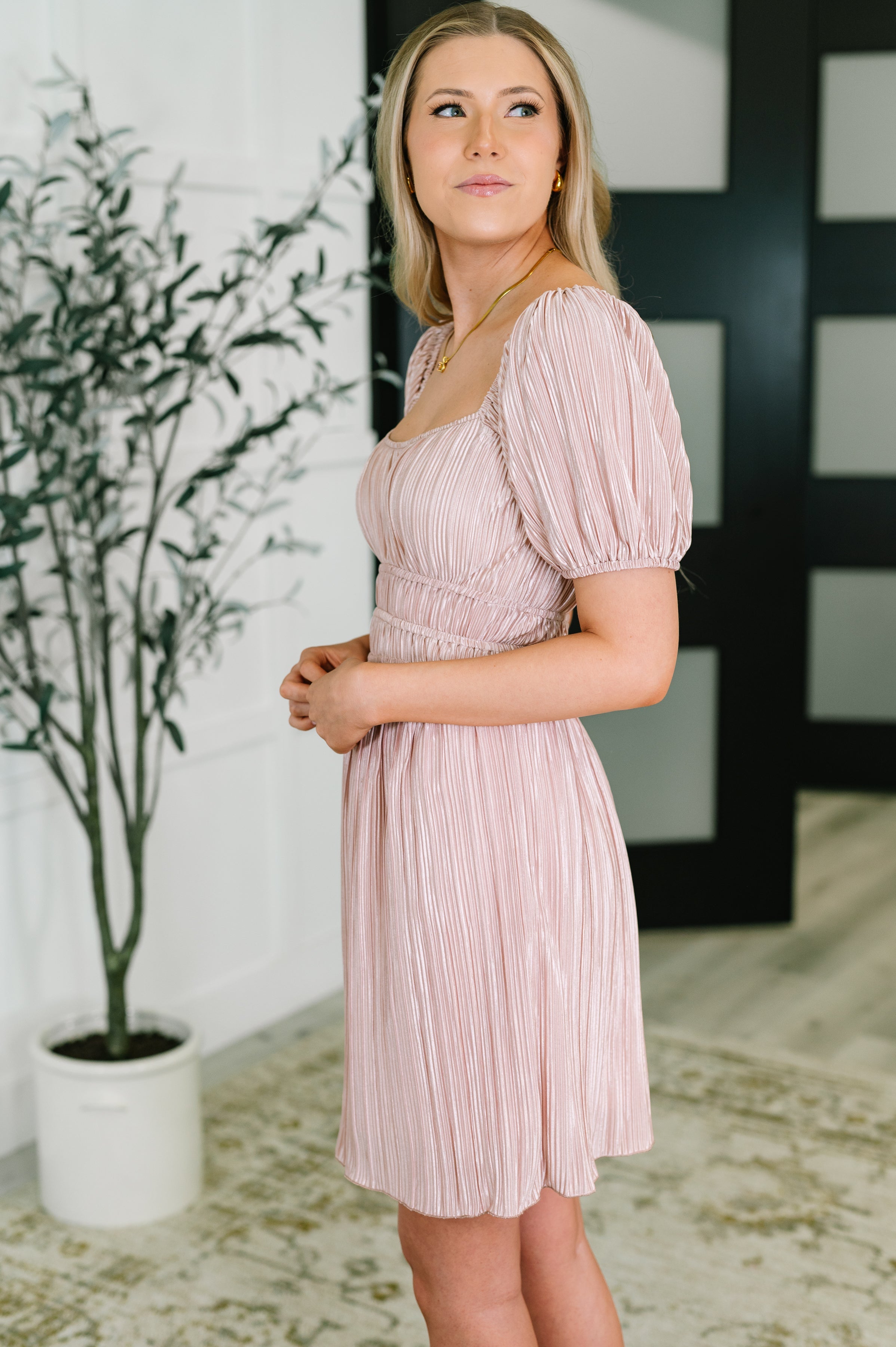 Woman wearing a soft pink pleated dress with puffed short sleeves and ruched waist standing indoors