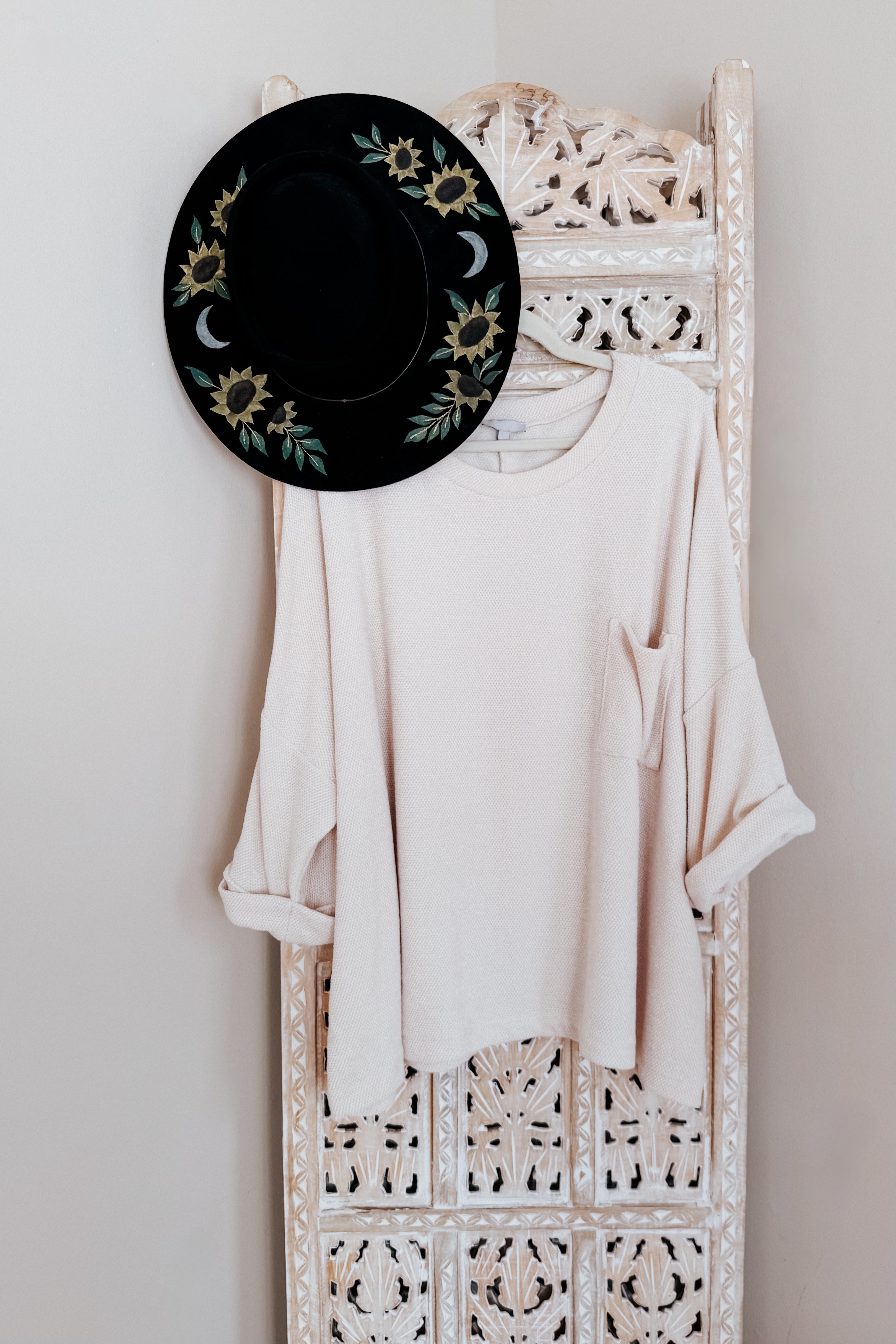 Ivory Thoughts chenille blouse with chest pocket and rolled sleeves hanging on carved wooden panel with black floral hat