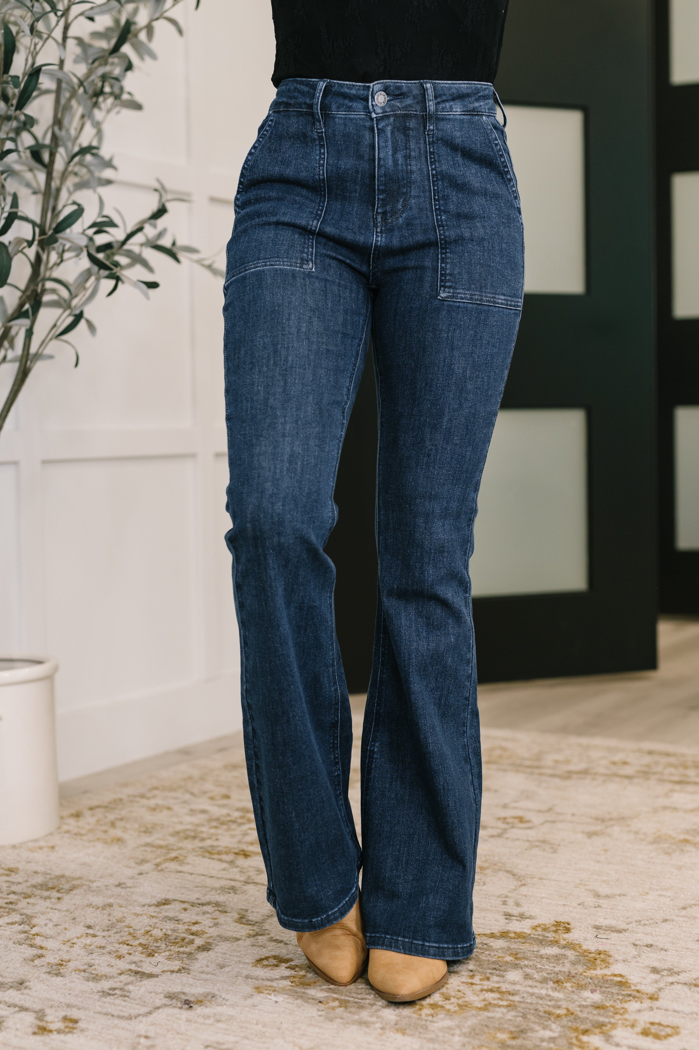 Front view of person wearing blue Jada high waist flare jeans featuring patch pockets and tan pointed shoes indoors