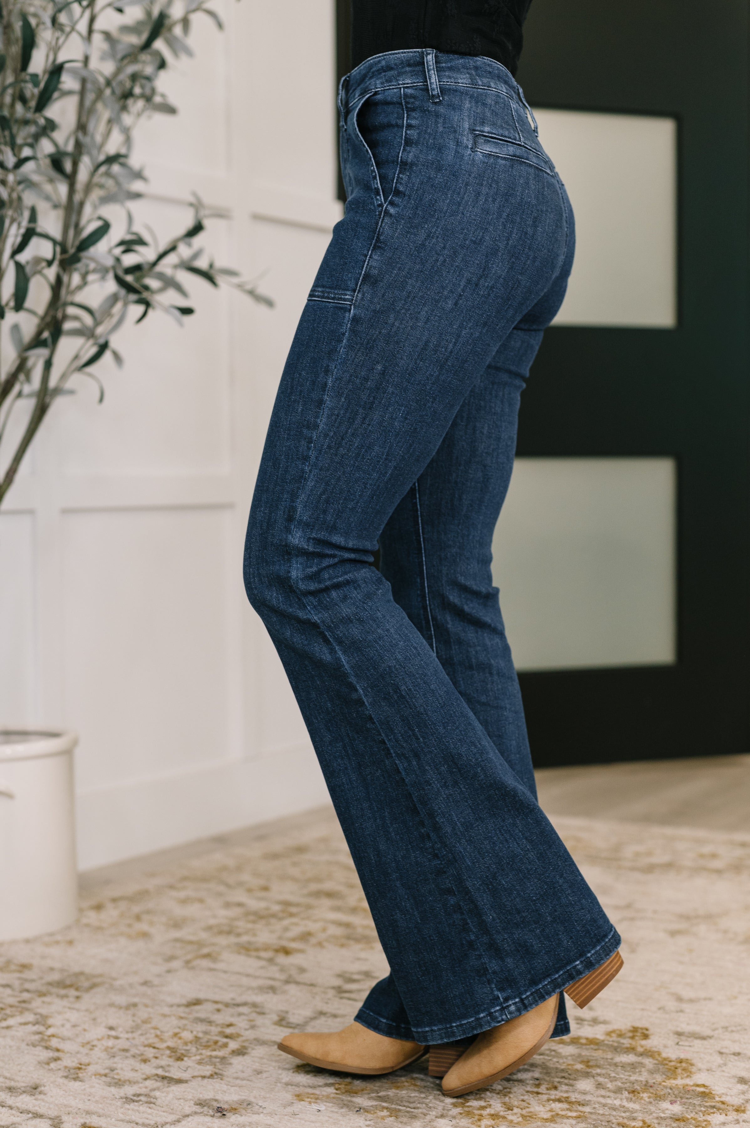 Side view of person wearing blue Jada high waist flare jeans with patch pockets and tan shoes indoors