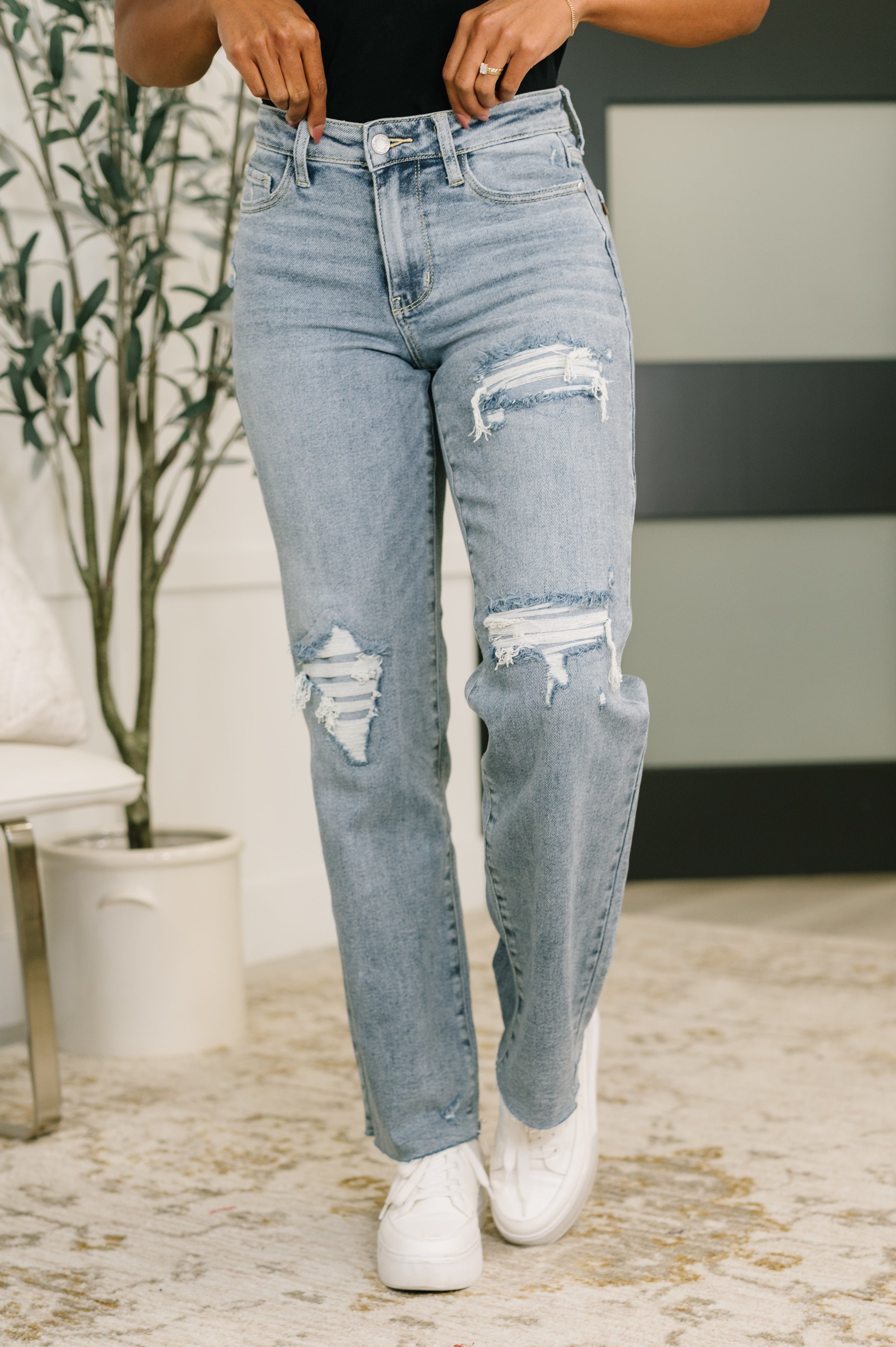 Woman wearing blue Jade Mid Rise 90's Straight jeans with ripped details on thighs and white sneakers indoors