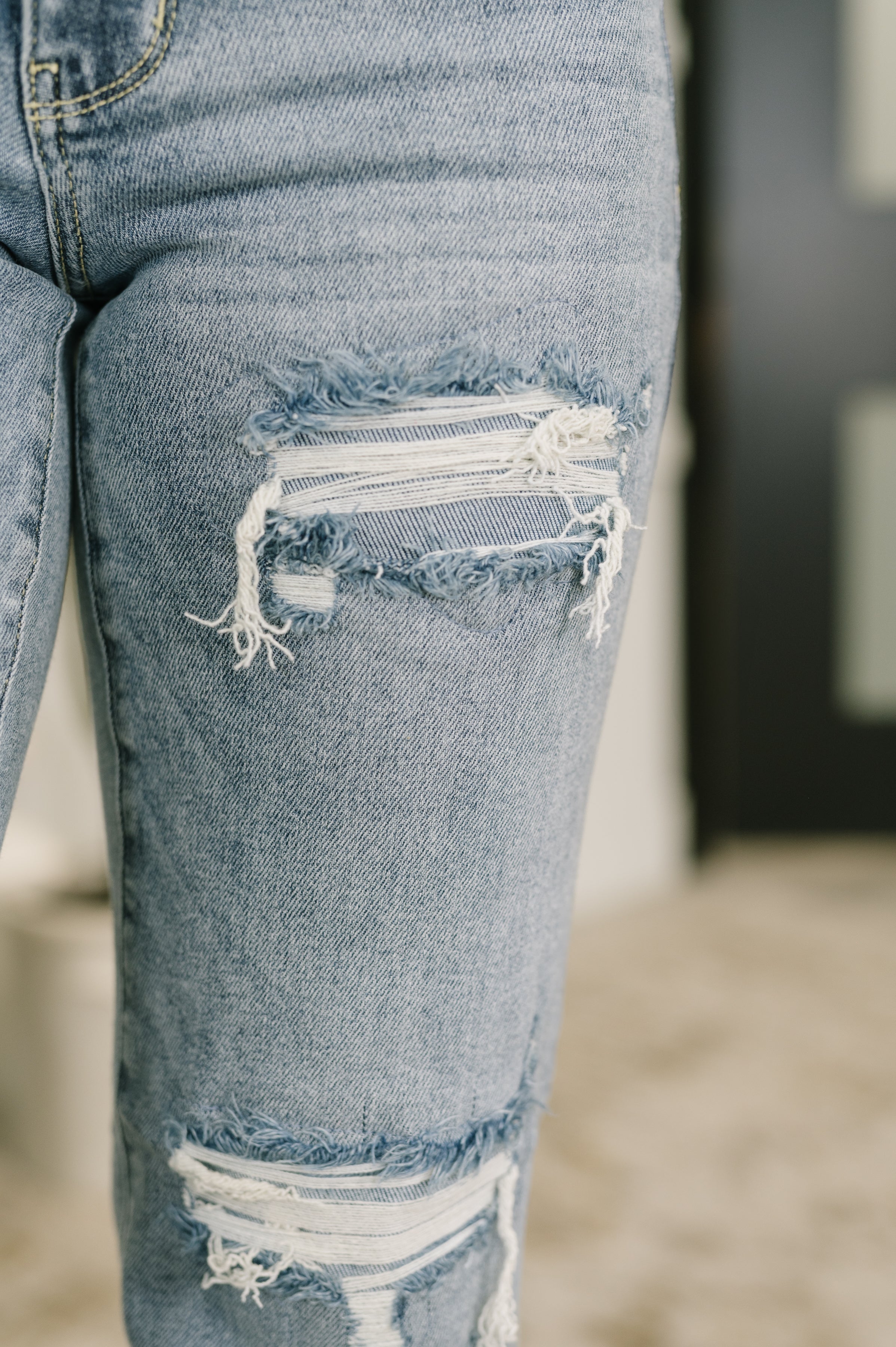 Close-up of distressed detailing on knee area of blue Jade Mid Rise 90's Straight jeans indoors