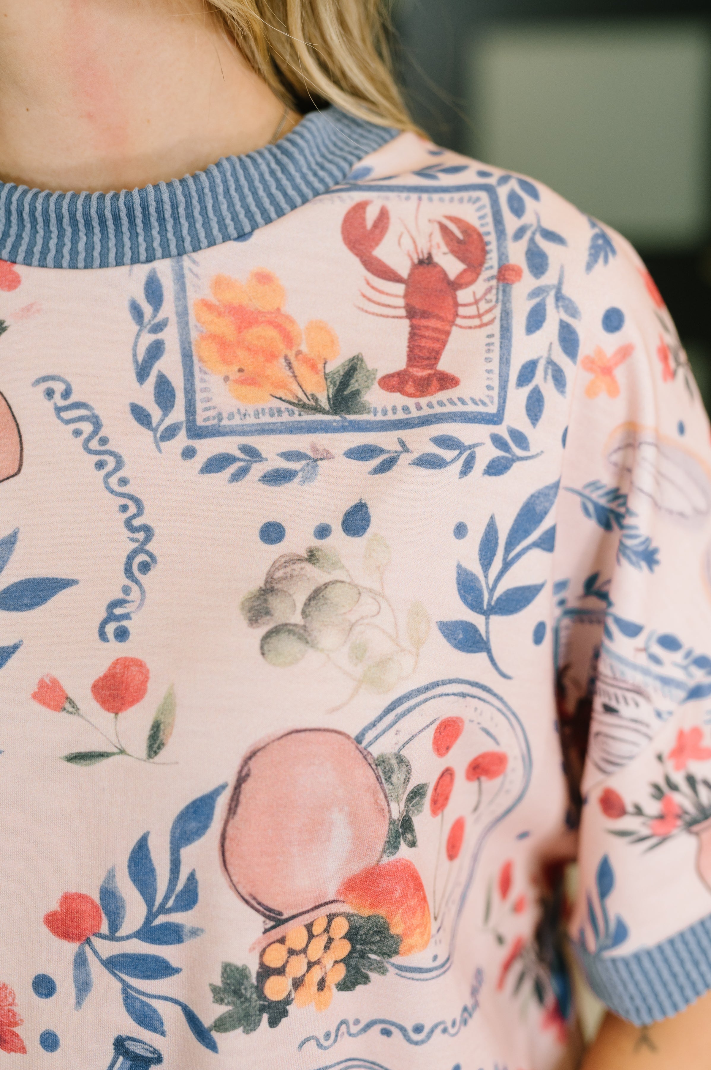 Close-up of cream top with blue ribbed collar featuring colorful floral and lobster graphic prints