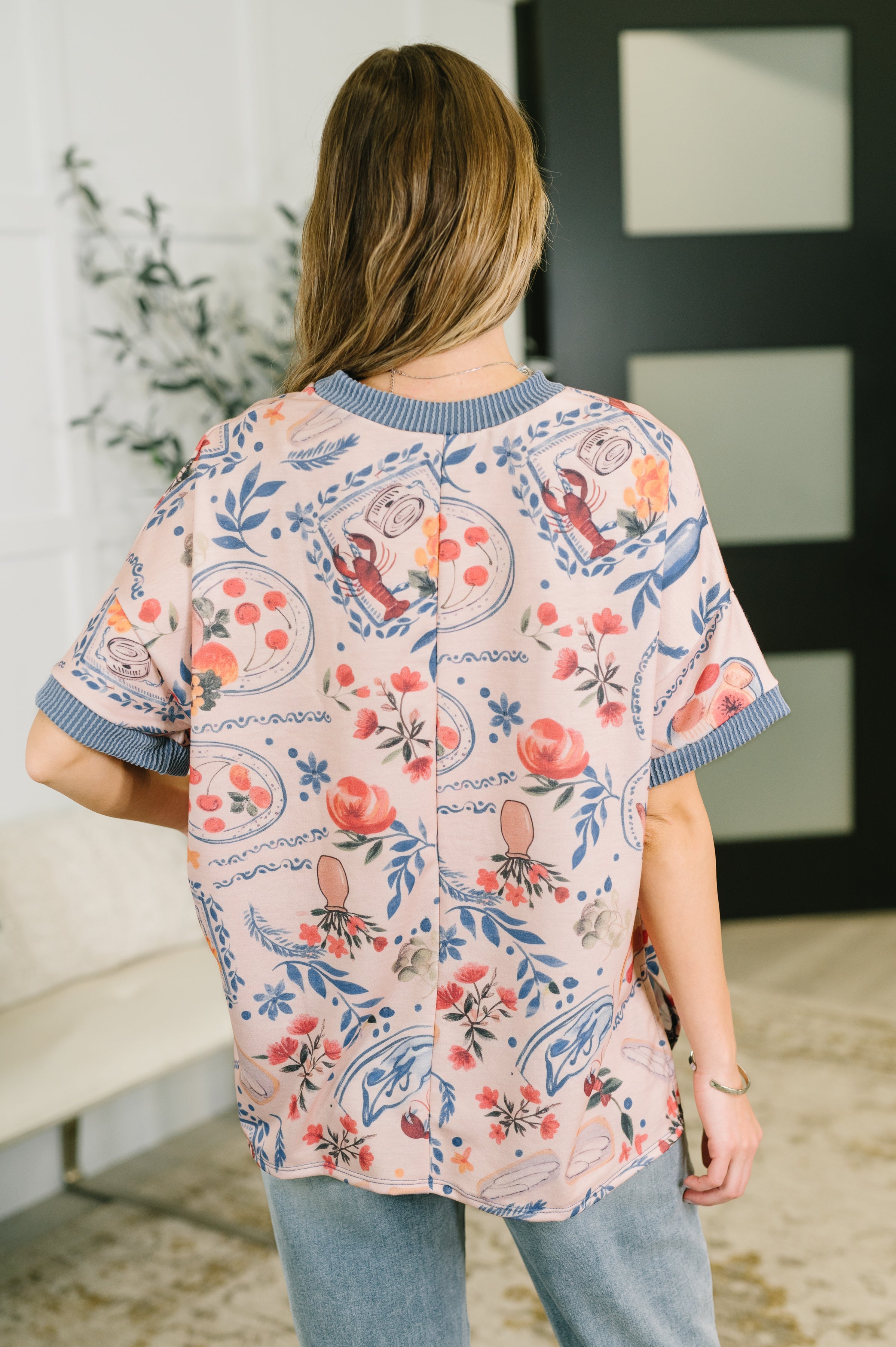 Back view of woman wearing a relaxed tee with blue ribbed cuffs and collar and colorful floral and lobster print indoors