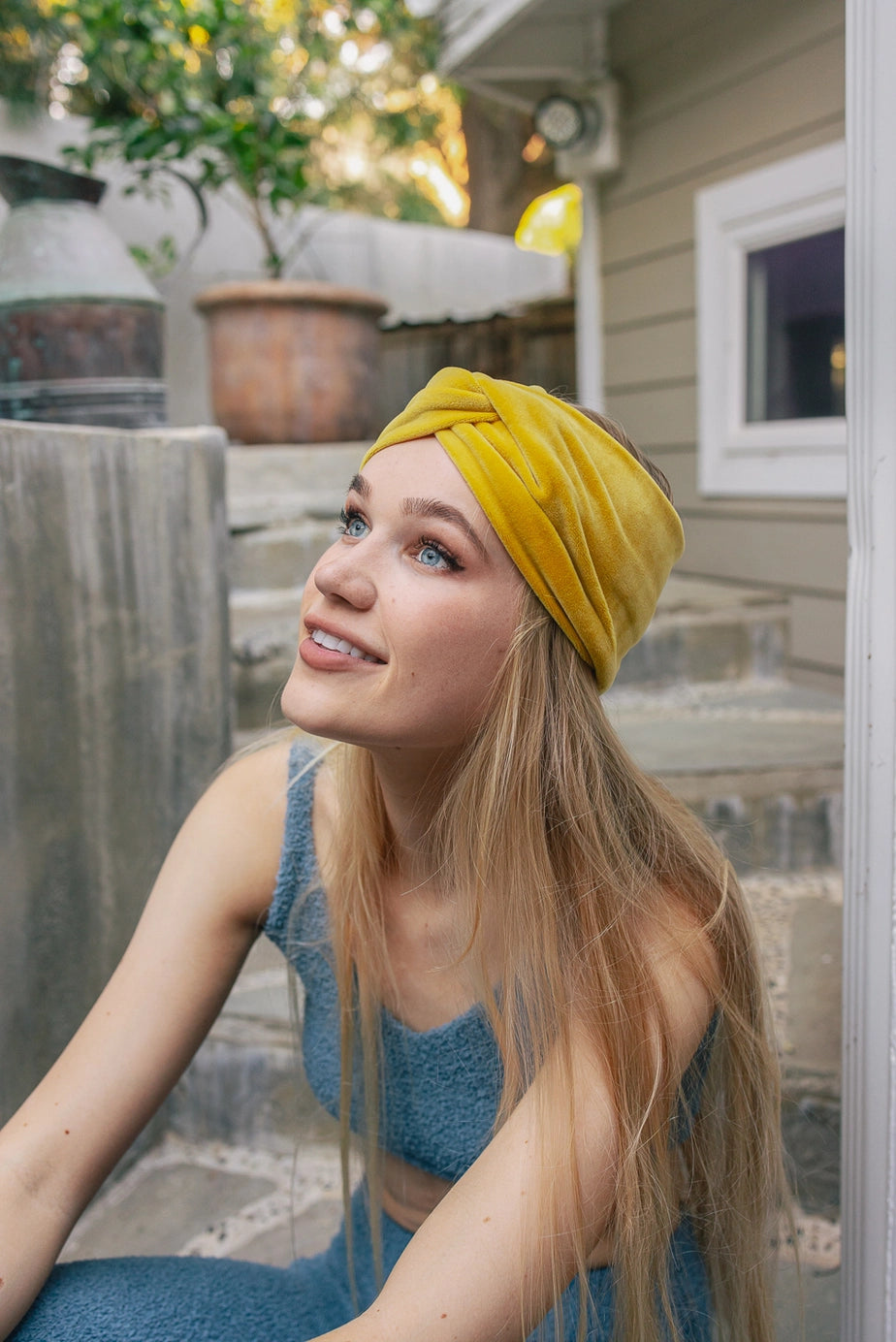 Young woman outdoors wearing sunflower-colored Joplin twisted velvet headband with long blonde hair and blue outfit