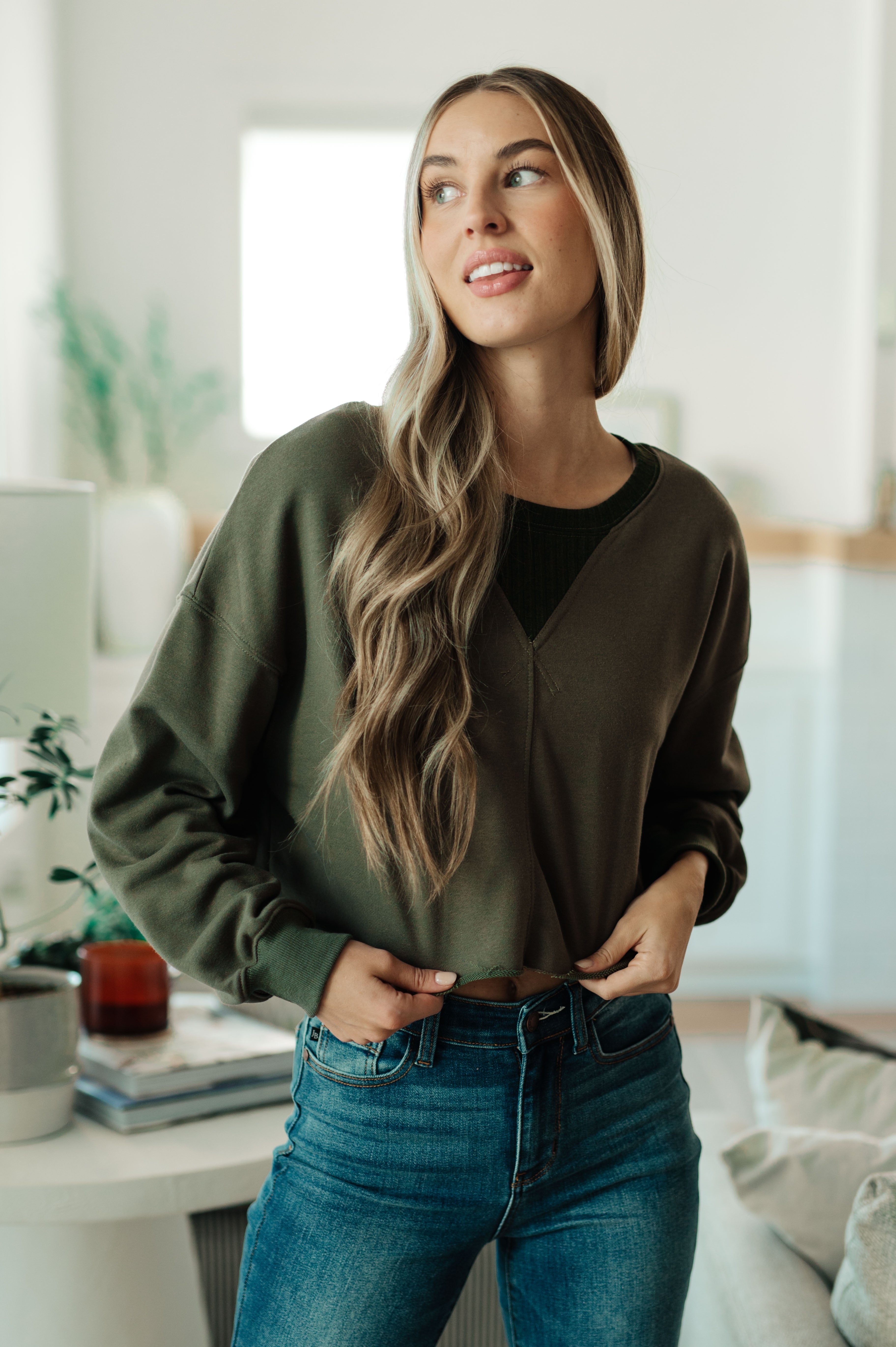 Woman indoors wearing green Just a Casual Crop Pullover with relaxed fit over black top and high-waisted blue jeans