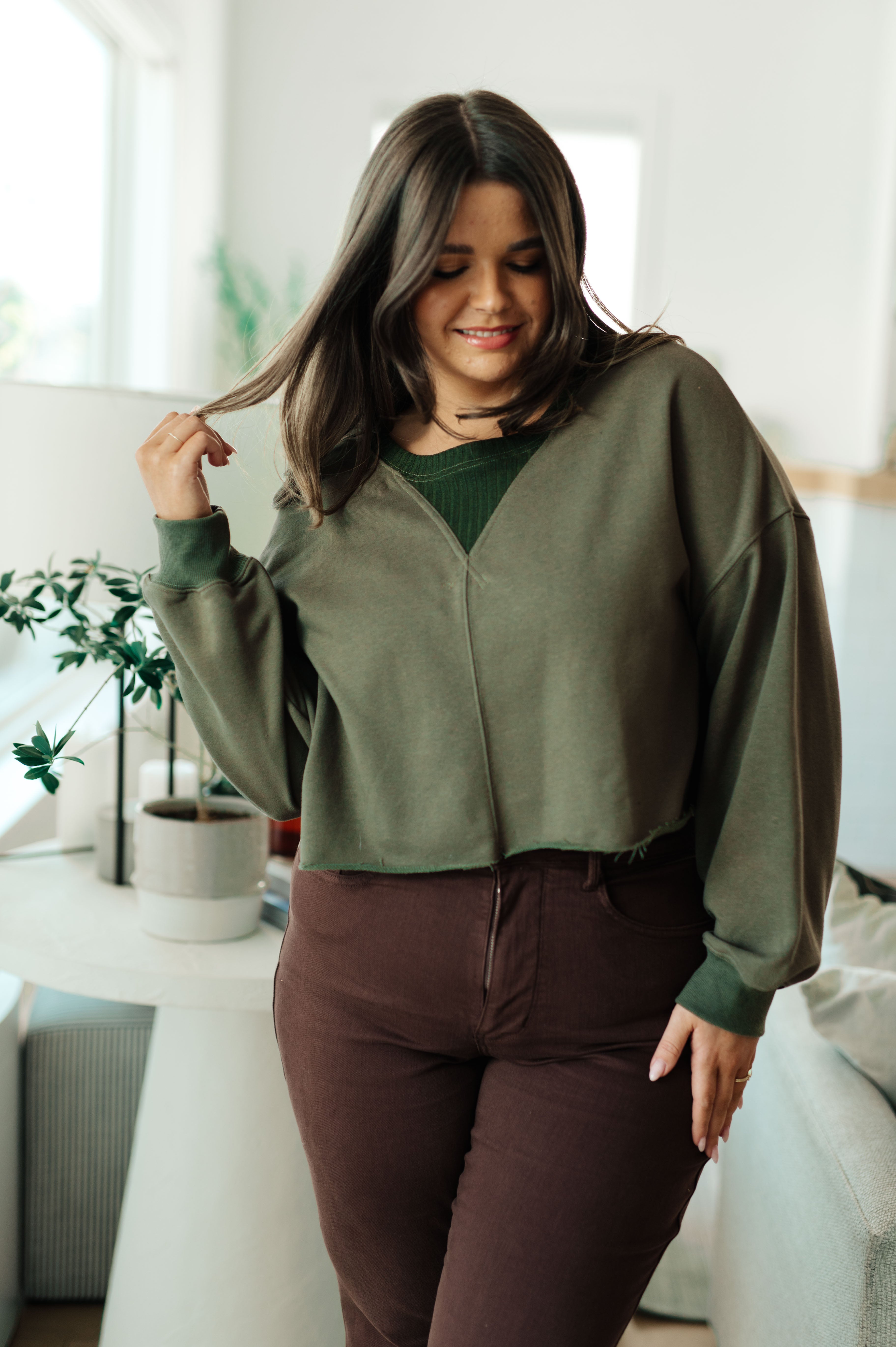 Woman indoors wearing green Just a Casual Crop Pullover with relaxed fit paired with high-waisted dark brown pants