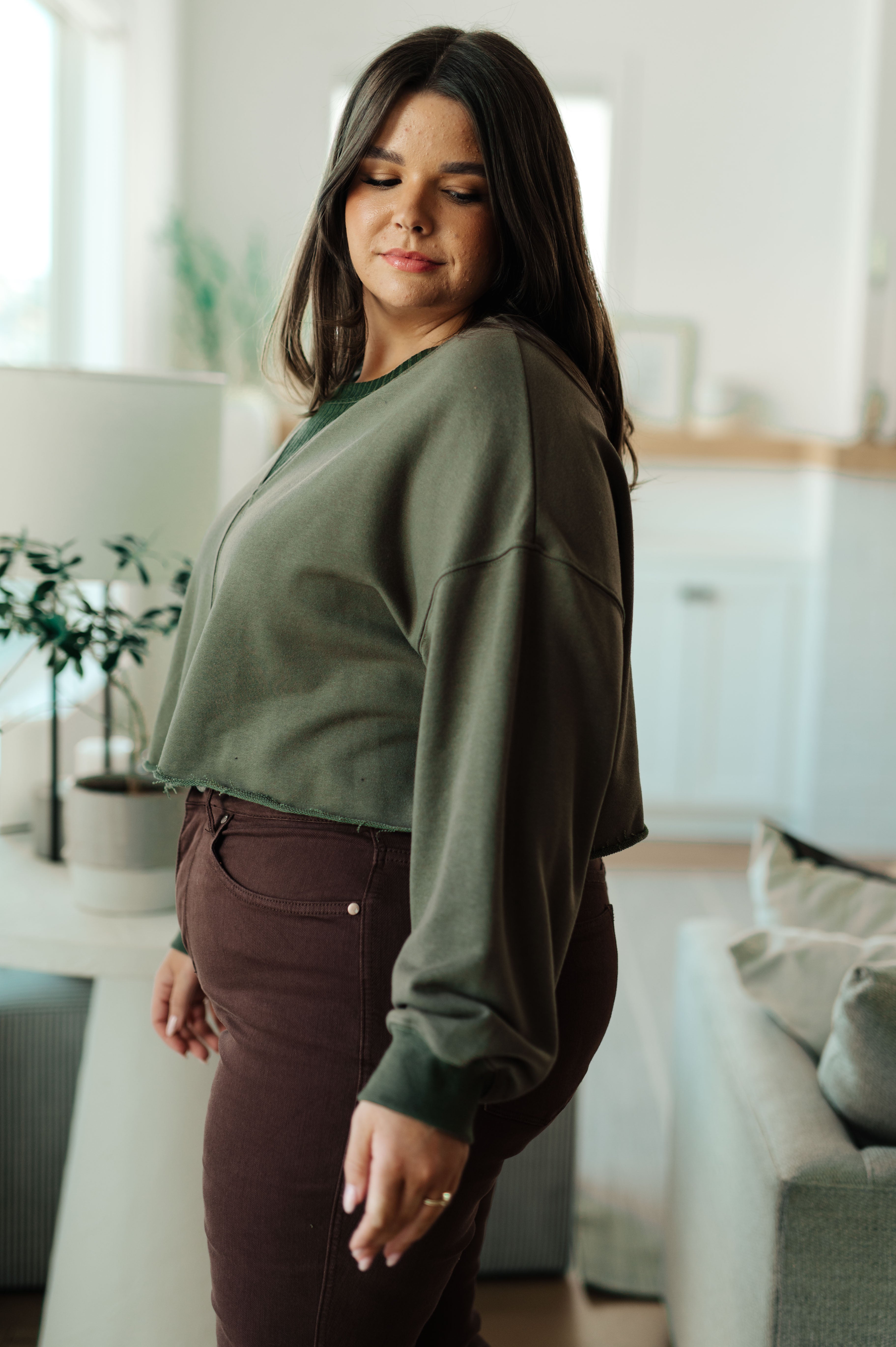 Side profile of woman indoors wearing green Just a Casual Crop Pullover paired with dark brown pants