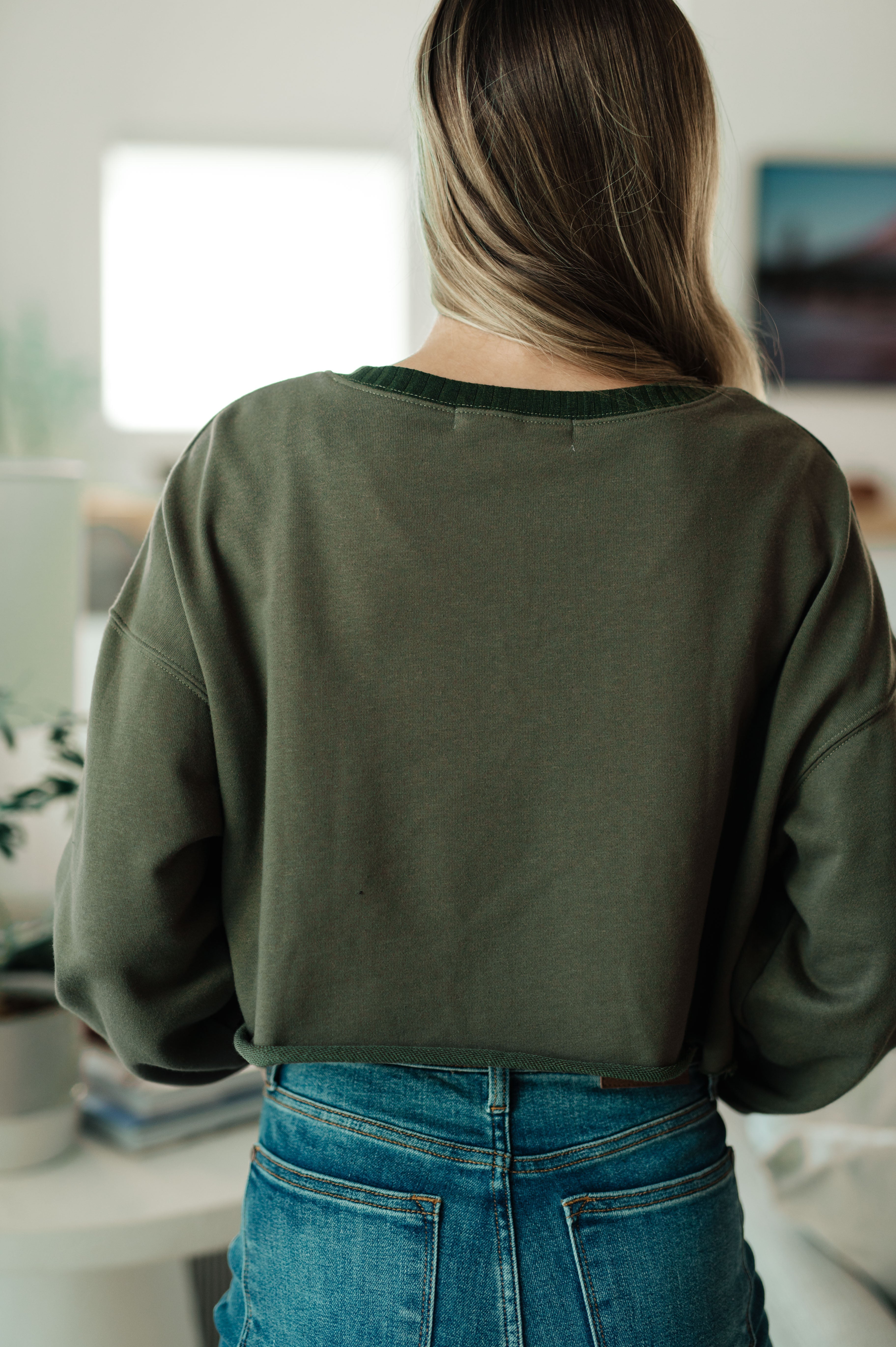 Back view of person indoors wearing green Just a Casual Crop Pullover paired with high-waisted blue jeans