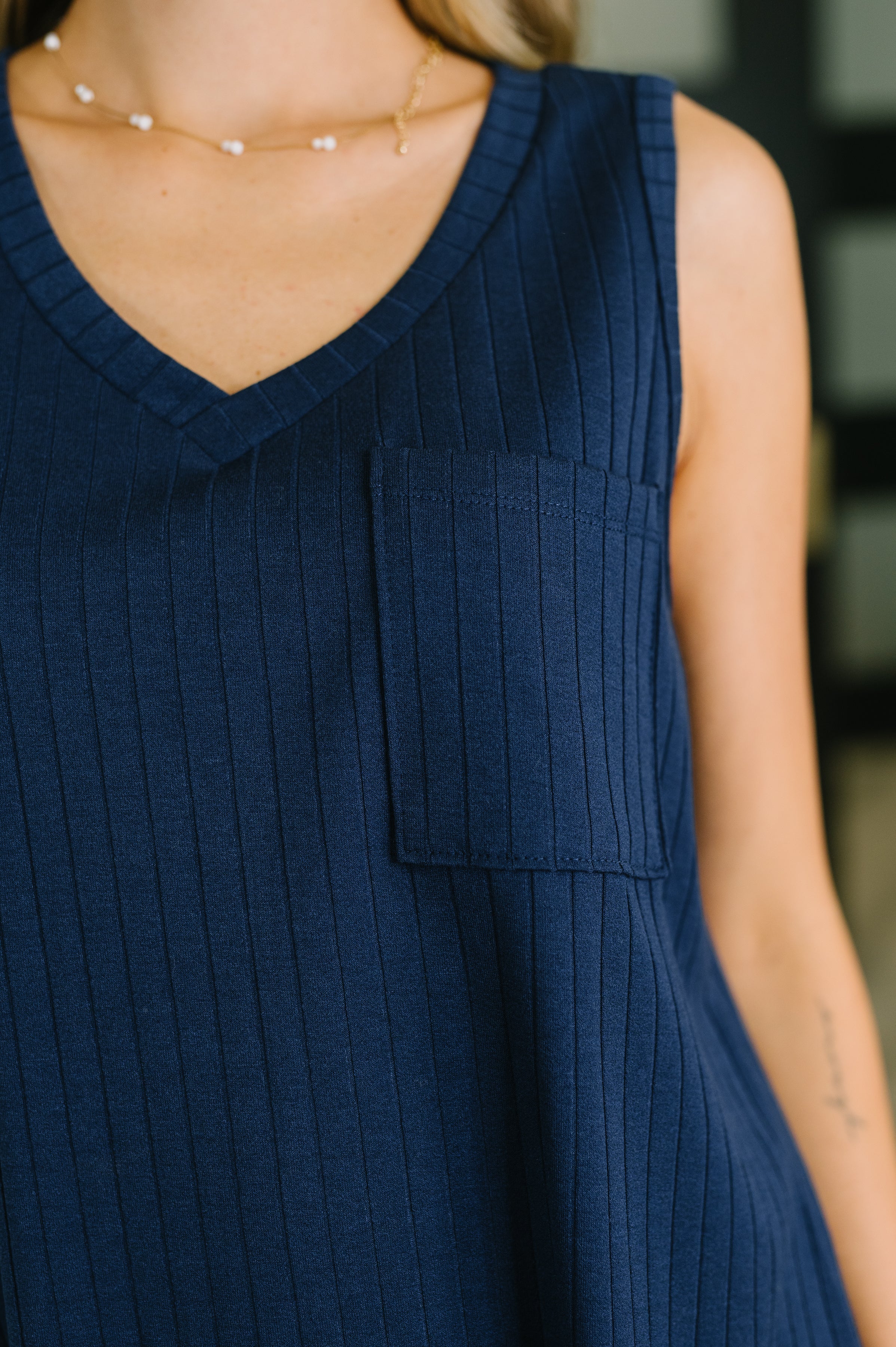 Close-up of navy ribbed knit tank with V-neck and chest pocket on woman wearing delicate layered necklace