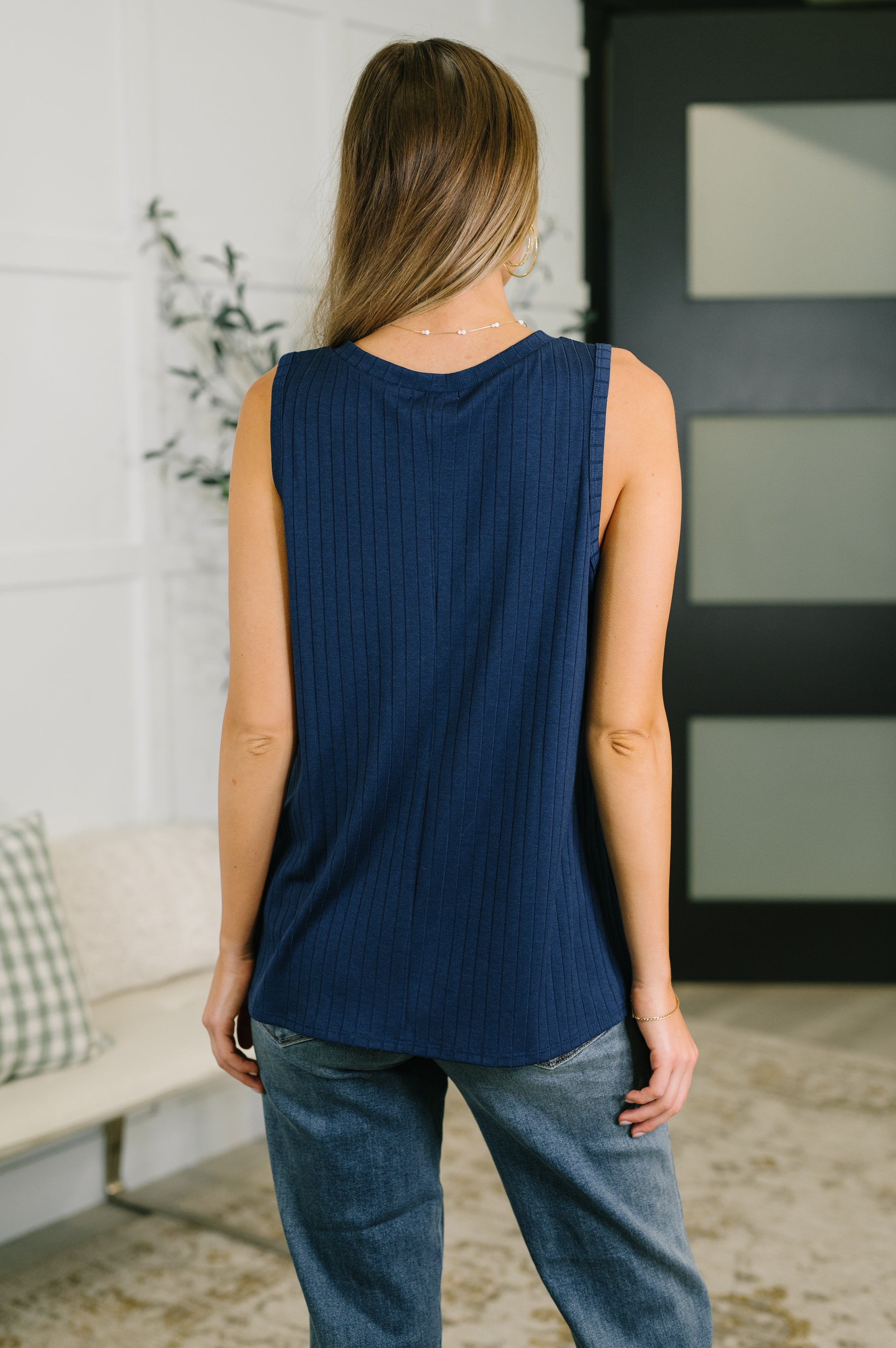 Rear view of woman wearing a navy ribbed knit tank with relaxed fit paired with casual jeans indoors