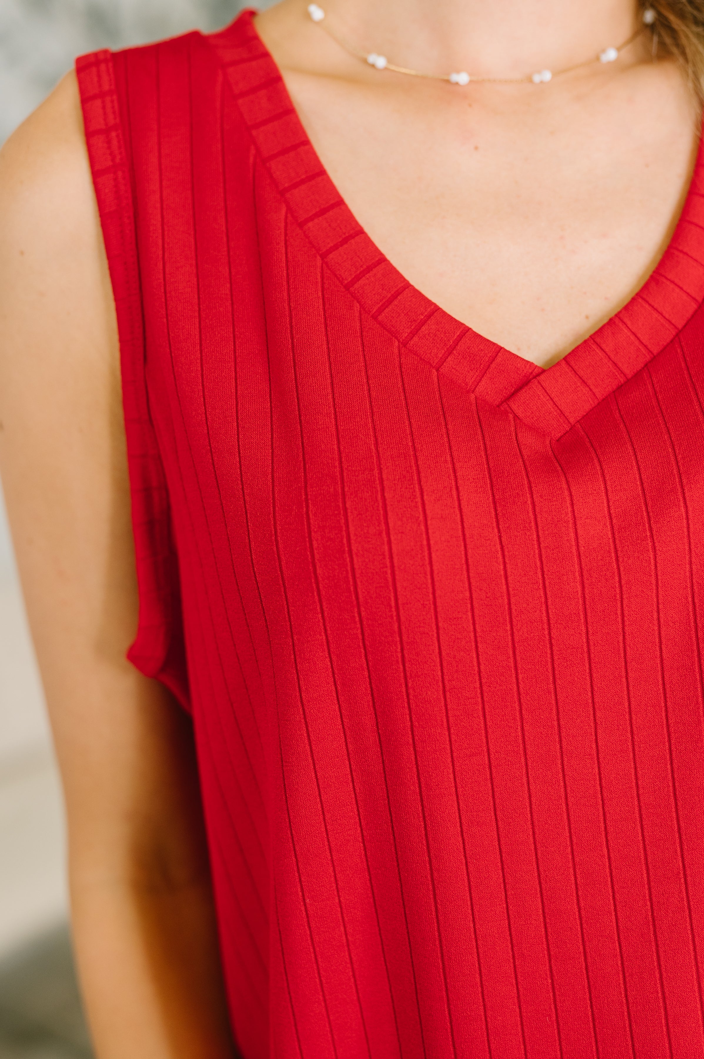 Close-up of red ribbed knit tank with V-neck worn with delicate beaded necklace on model's bare shoulders