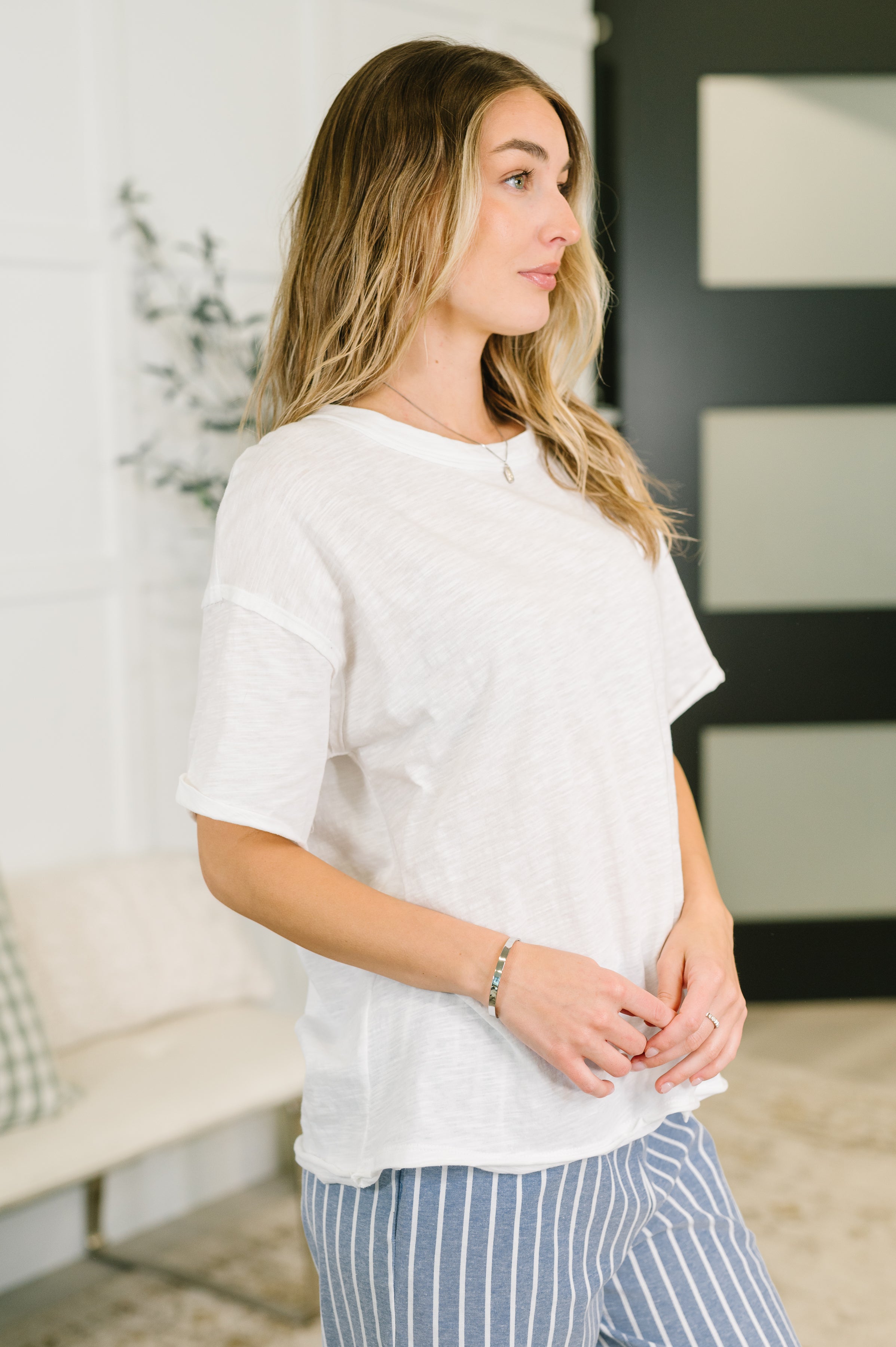 Woman wearing relaxed ivory heather tee paired with blue and white striped pants in bright indoor setting