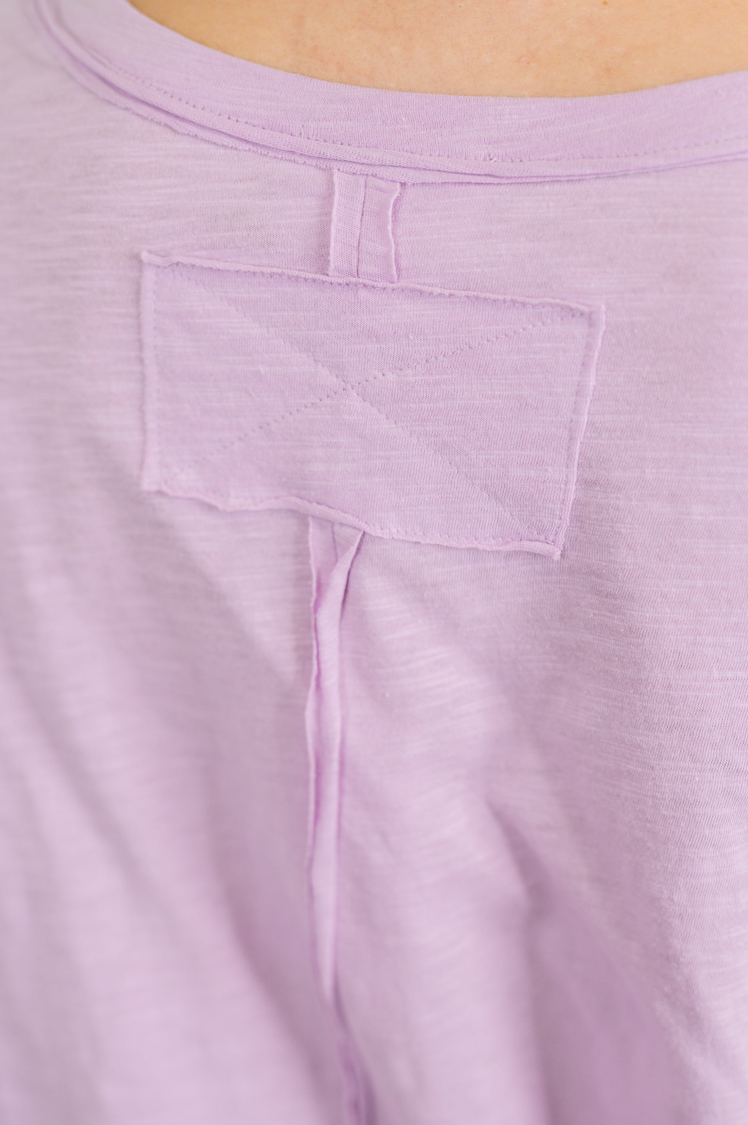Close-up of lilac relaxed tee fabric with visible stitched patch detail on back collar area