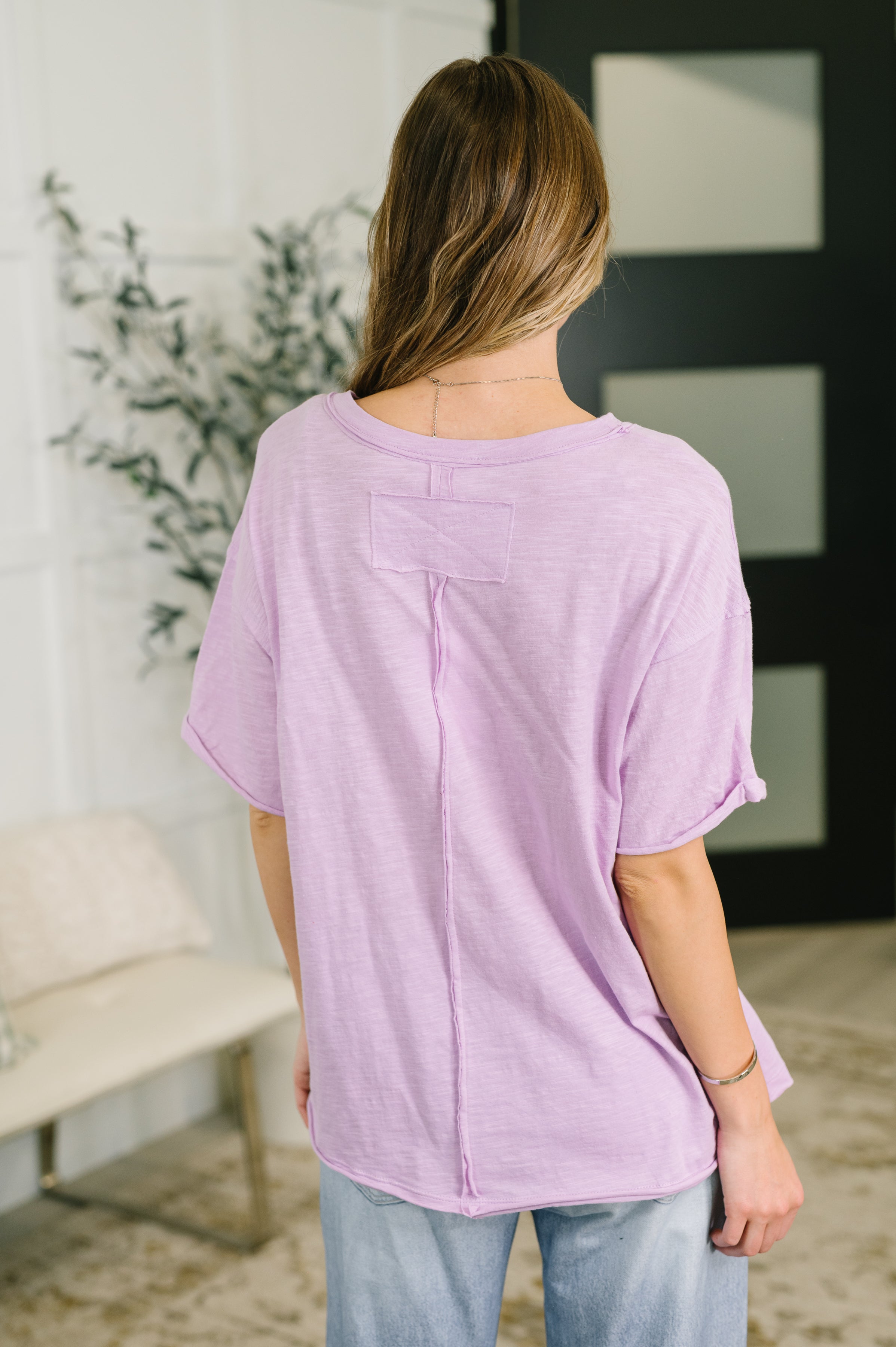 Woman wearing relaxed lilac heather tee with raw seam detail styled with light wash jeans indoors