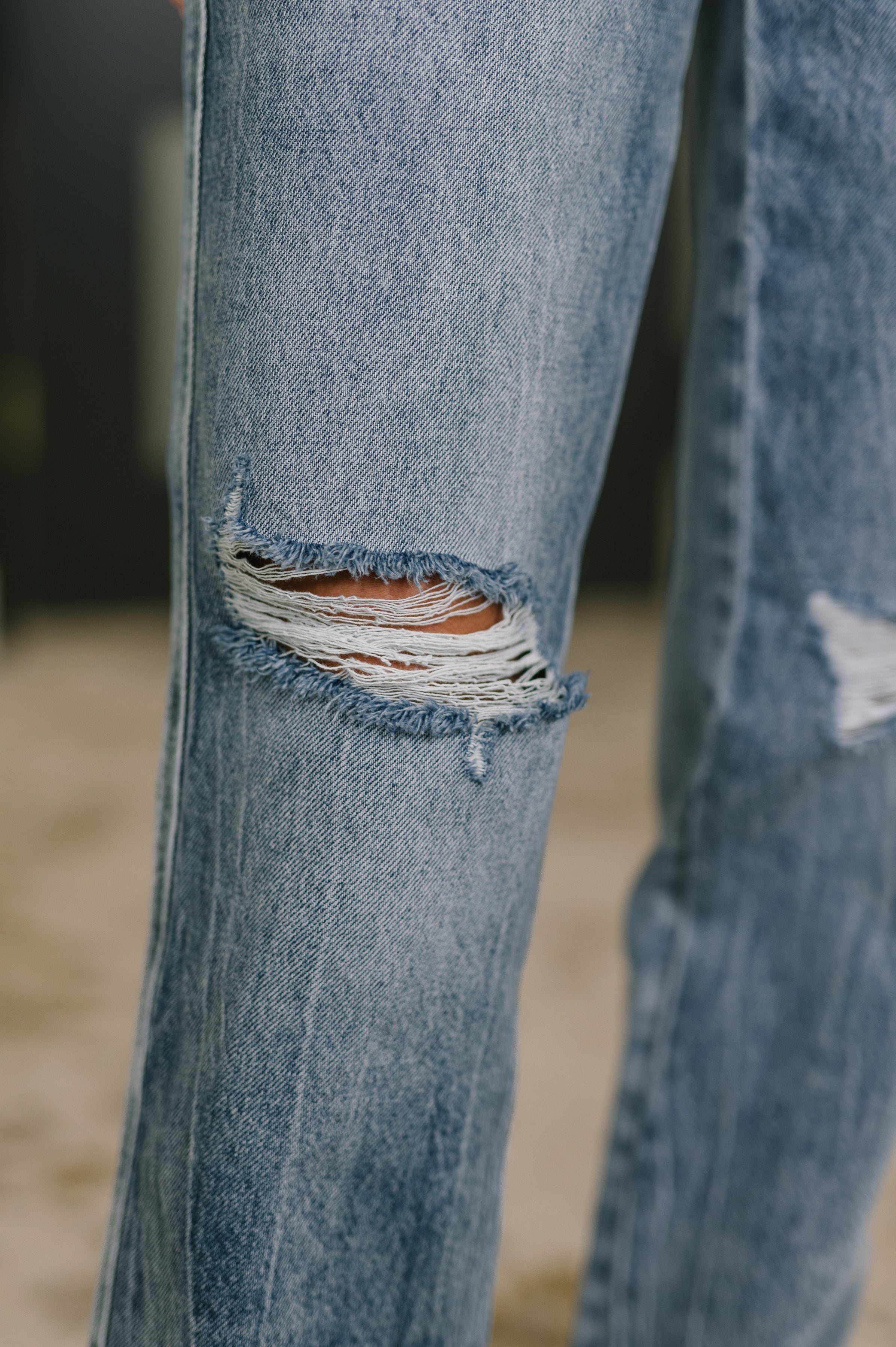 Close-up of light blue high waist rigid straight jeans with distressed rip detail on the knee area indoors