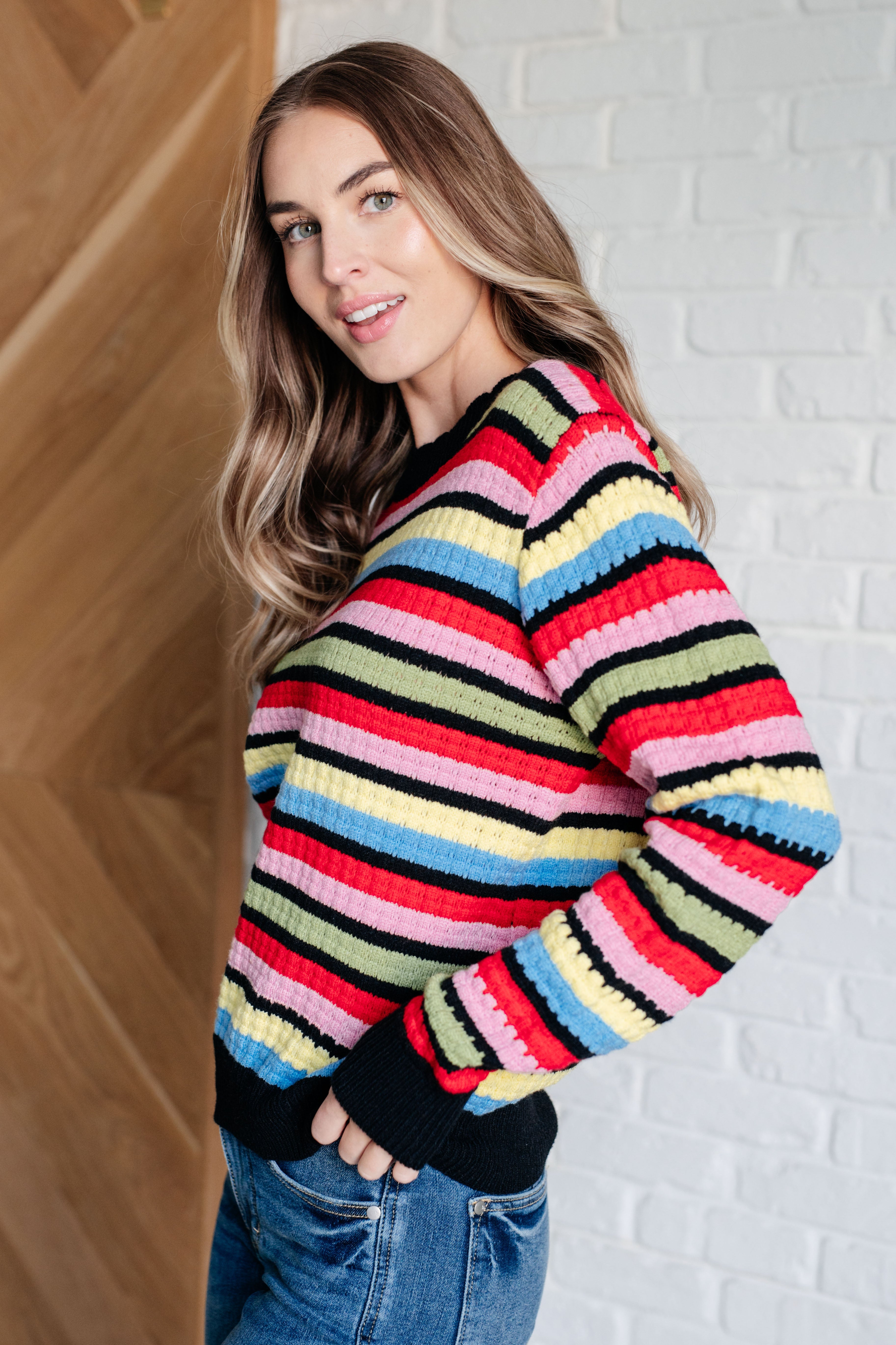 Side view of woman wearing multicolor Keep Dreaming Striped Sweater with ribbed cuffs and black hemline indoors