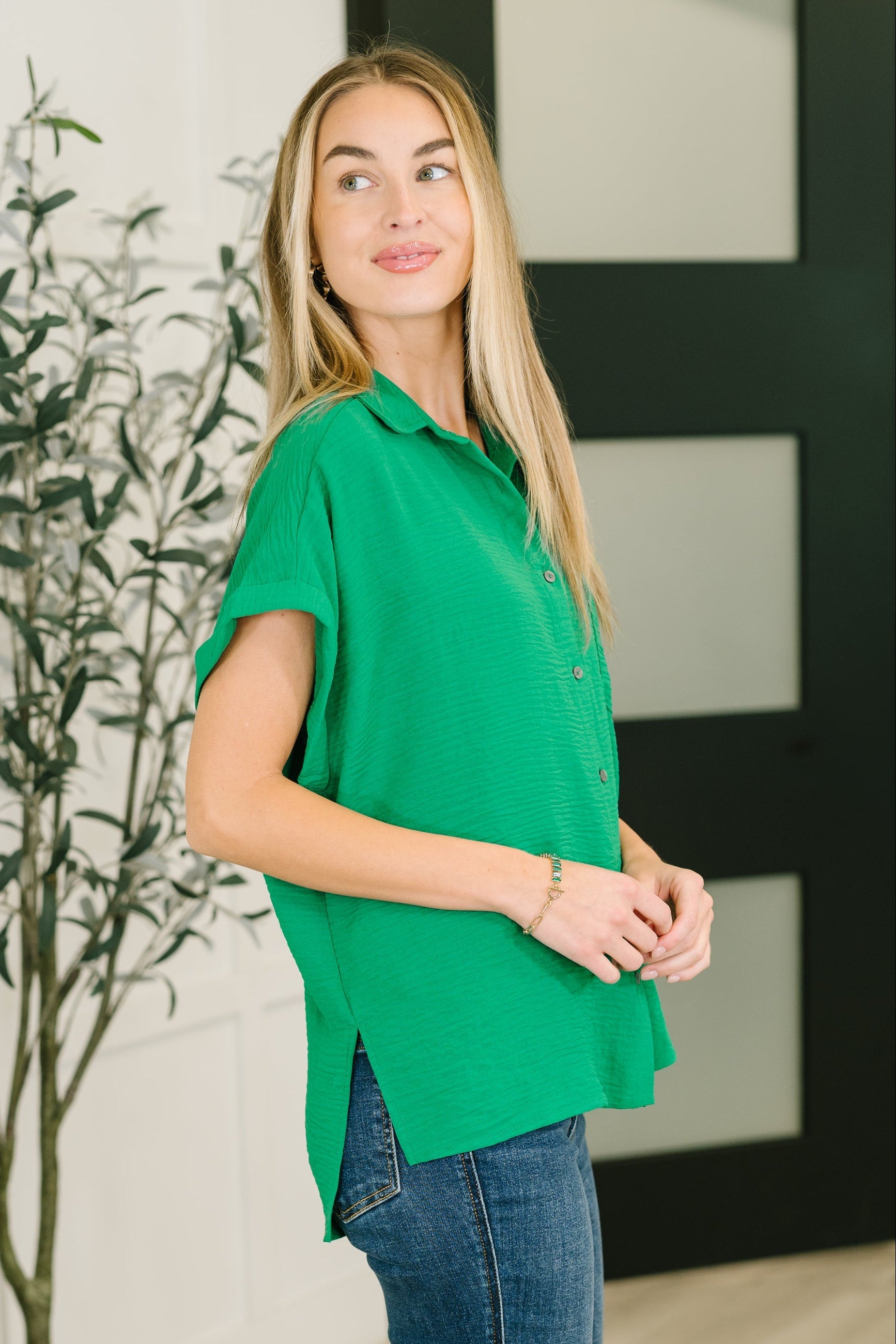 Blonde woman wearing loose fit bright green collared button-down shirt with short sleeves and side slits indoors