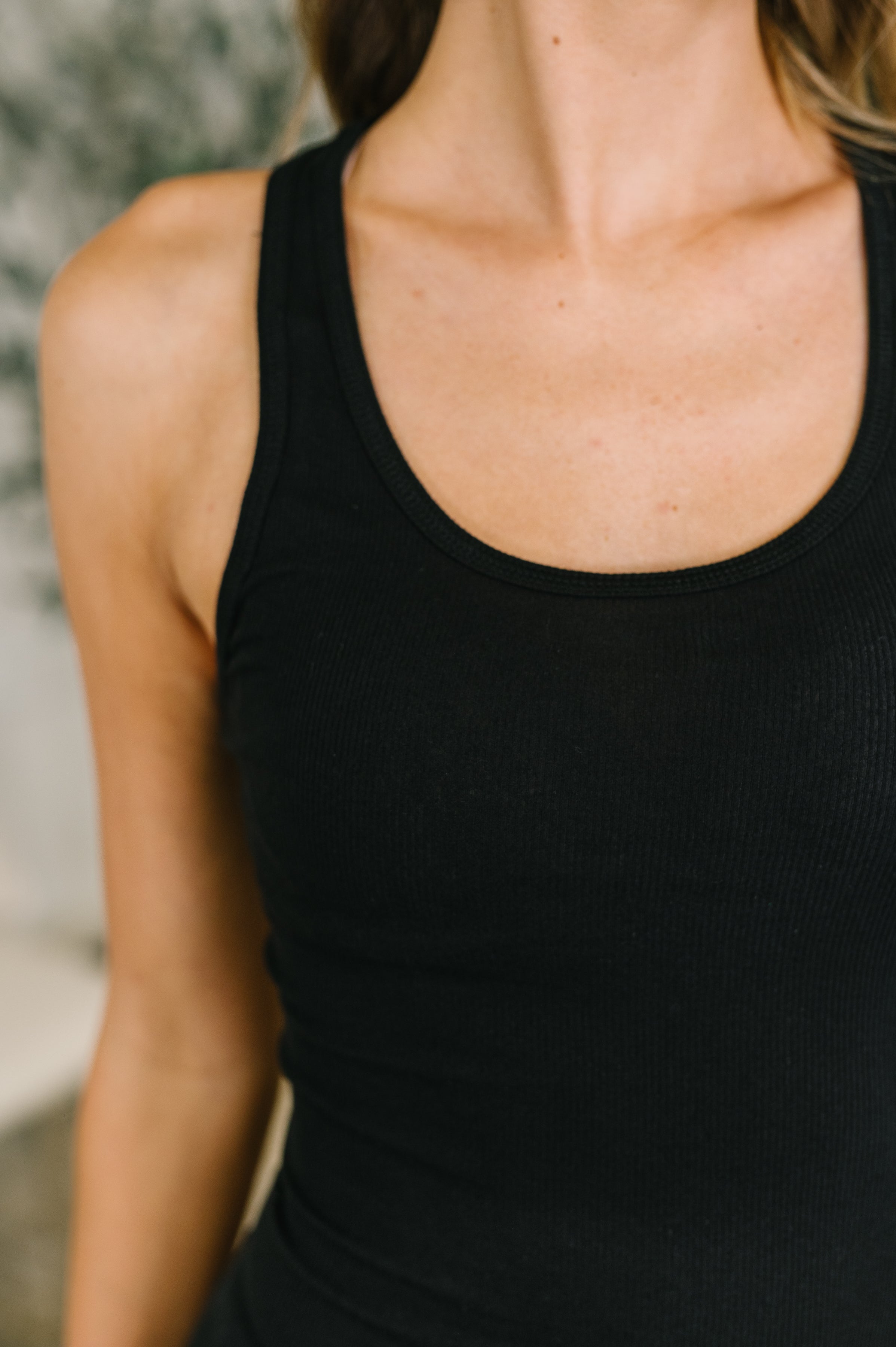 Close-up of black scoop neck tank top highlighting fitted style and soft ribbed fabric on woman’s upper torso