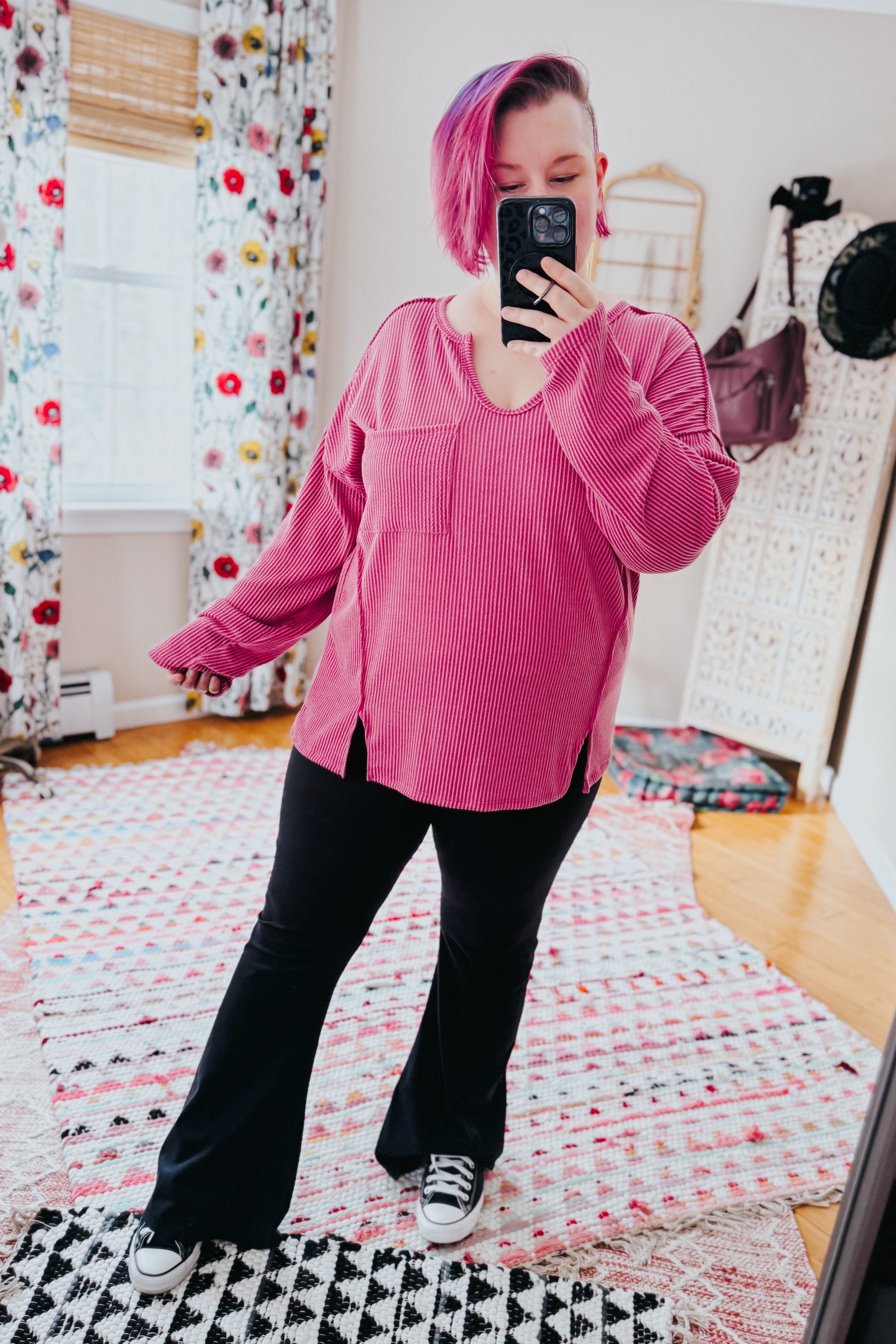 Woman with short pink hair taking a mirror selfie wearing a magenta ribbed top with front pocket and side slits