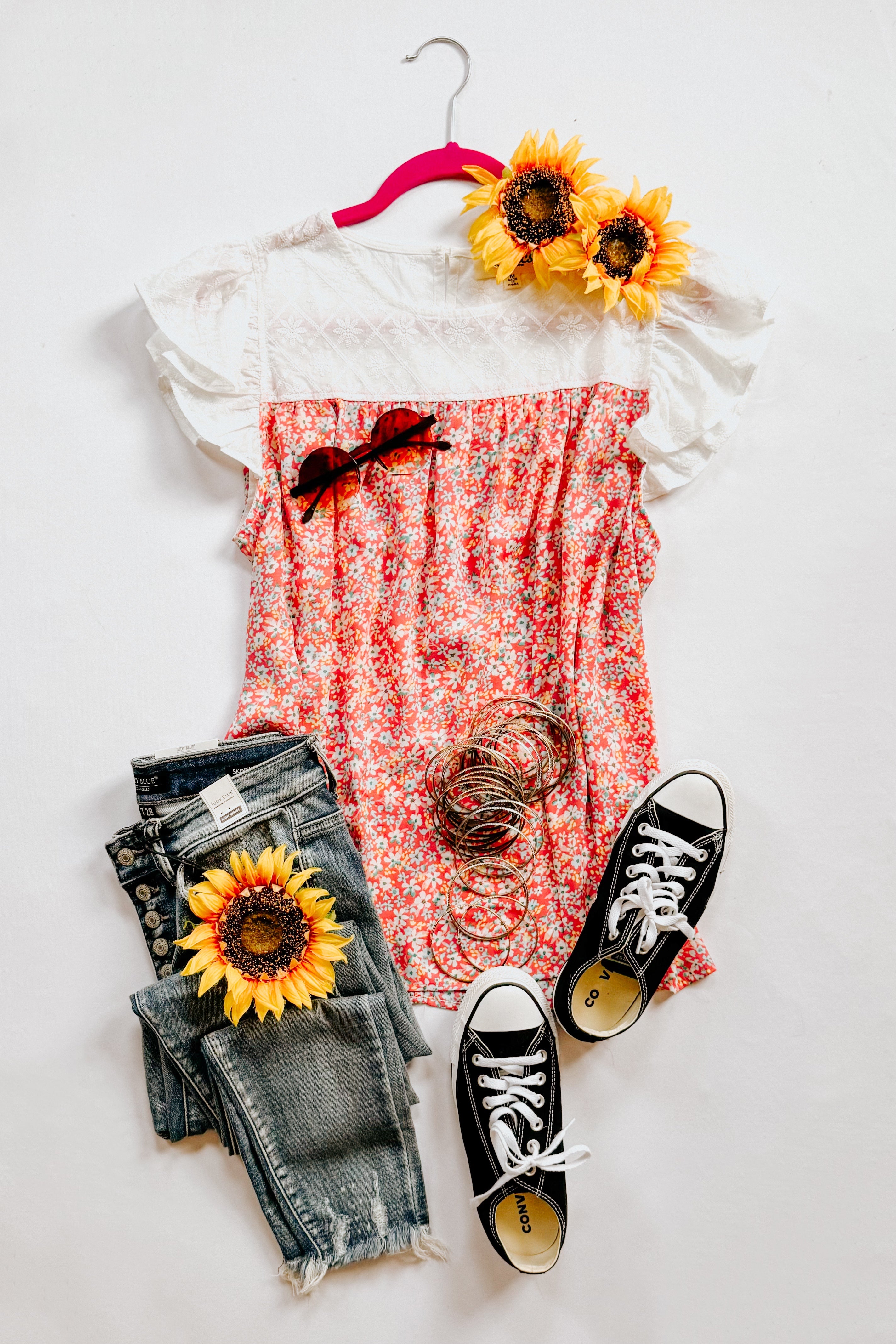 Pink floral blouse with white lace yoke paired with distressed gray jeans, black sneakers, and sunflower accents