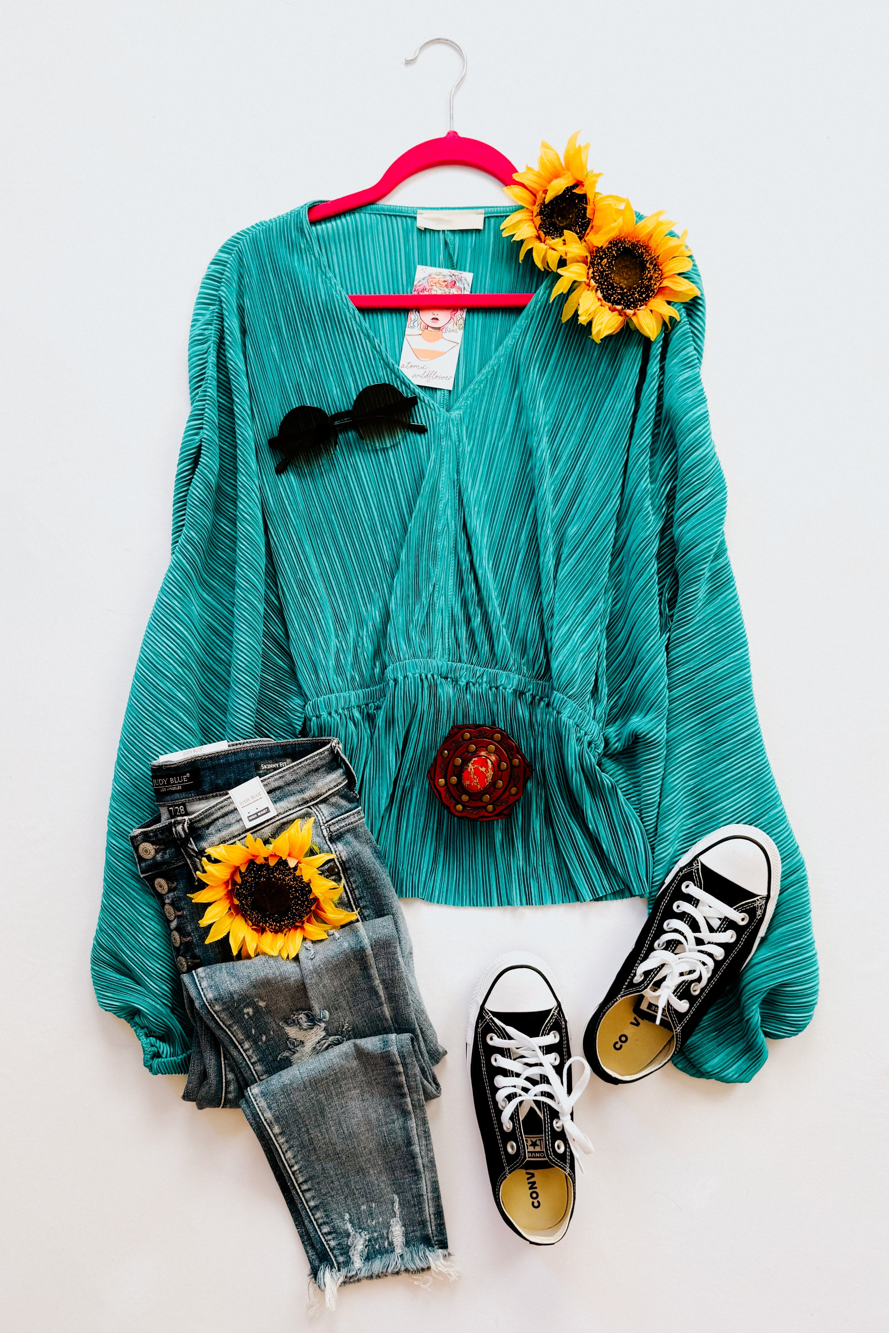 Teal pleated blouse with long puffed sleeves styled with distressed denim jeans, black sneakers, and bright sunflower accents