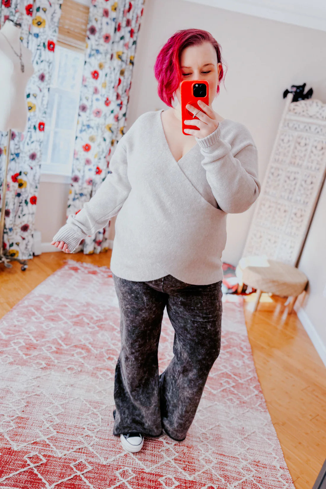 Woman with short magenta hair modeling a soft grey wrap sweater paired with wide-leg black pants indoors