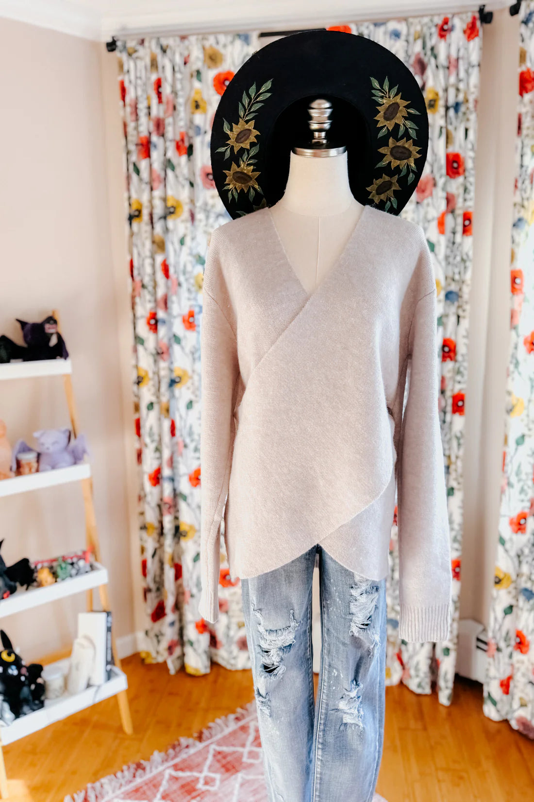 Soft grey knit sweater with an asymmetrical wrap front paired with distressed light wash denim jeans indoors