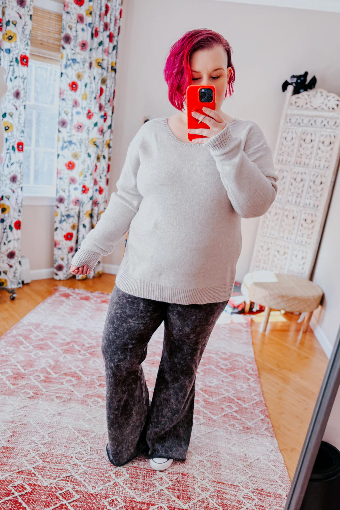 Woman with short magenta hair wearing a cozy grey long-sleeve sweater paired with dark grey wide-leg pants indoors