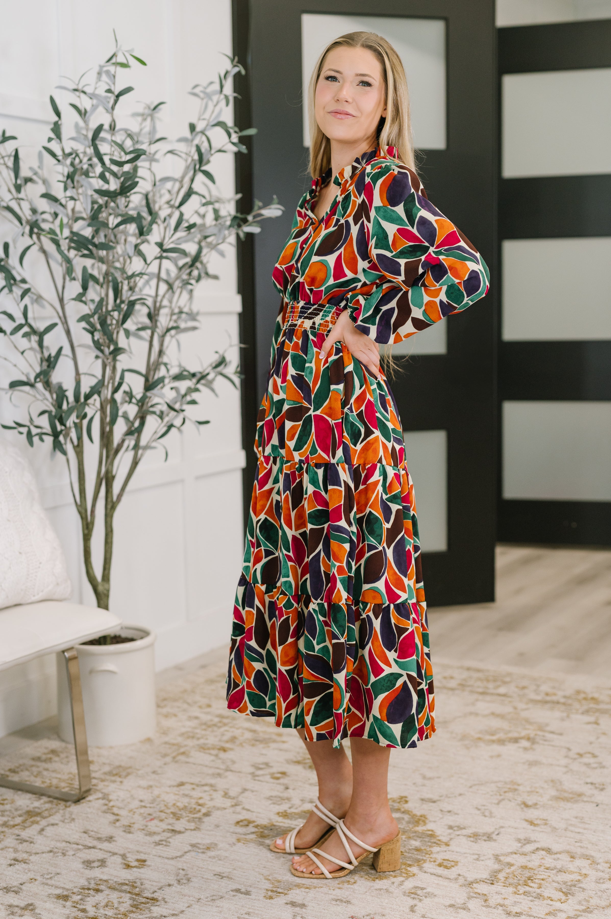 Woman wearing a vibrant leaf-patterned long sleeve tiered dress with a gathered waist standing indoors