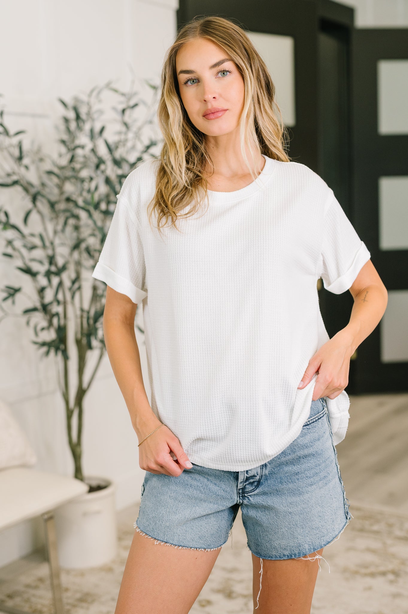 Woman wearing ivory waffle knit relaxed tee styled with light denim shorts in a bright, eclectic room environment