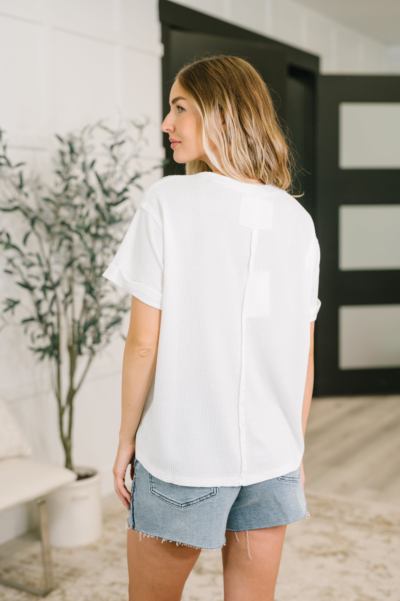 Woman seen from behind wearing a relaxed fit ivory waffle knit tee paired with casual denim shorts in a bright setting