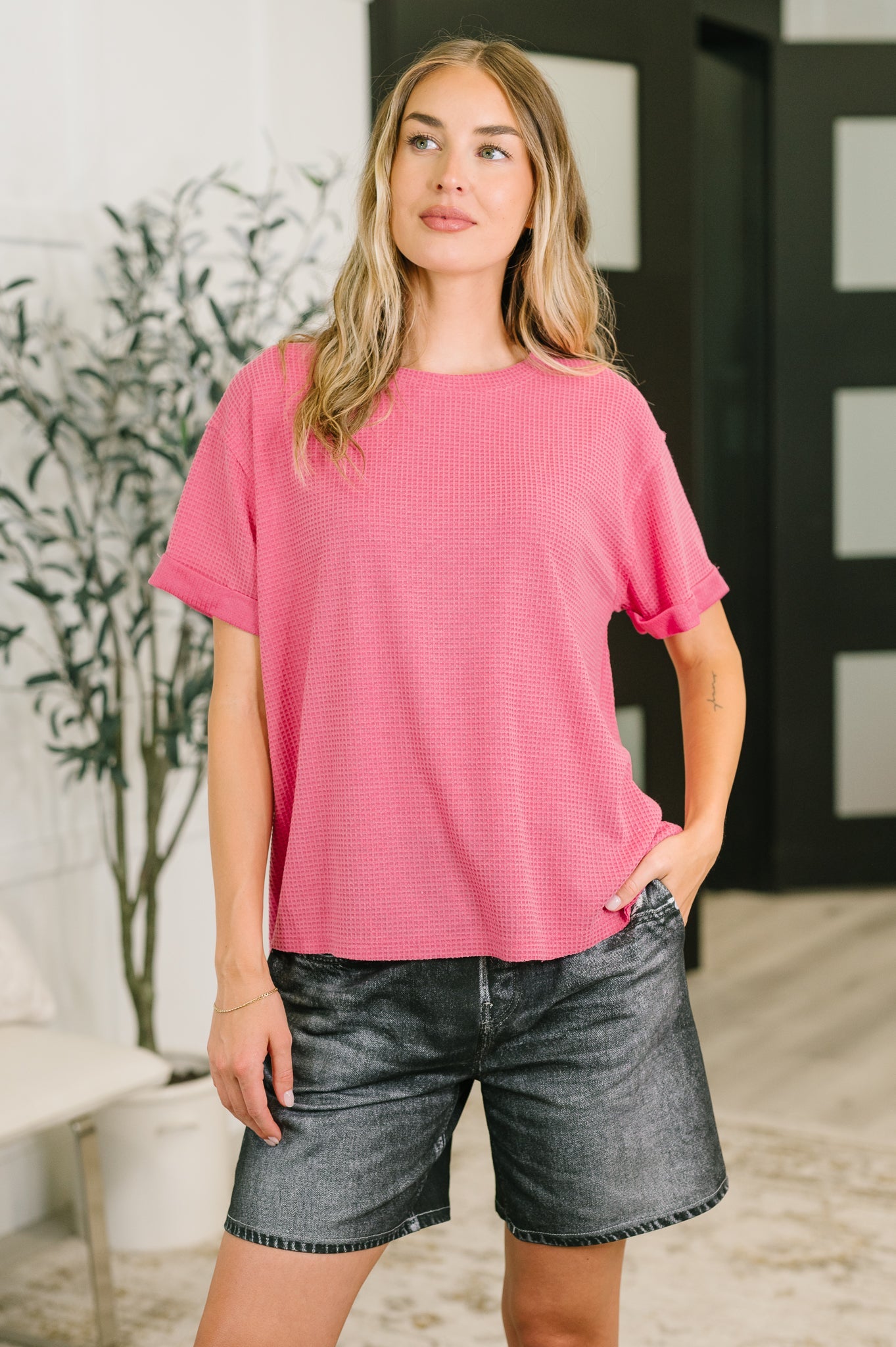 Woman wearing relaxed pink waffle knit tee with cuffed sleeves and black denim shorts in eclectic indoor setting