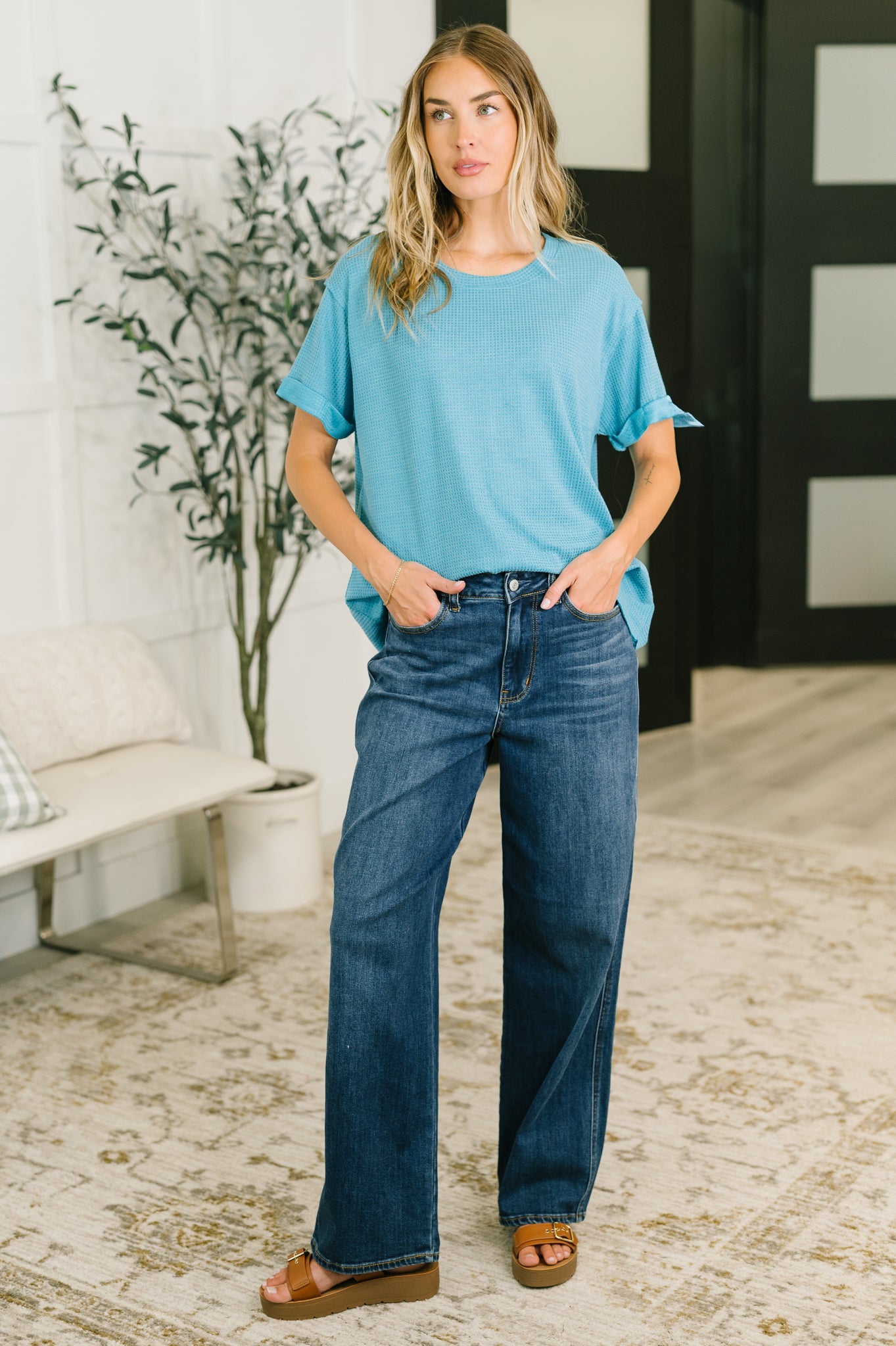 Woman wearing teal waffle knit relaxed tee with cuffed sleeves paired with wide-leg denim jeans and brown sandals