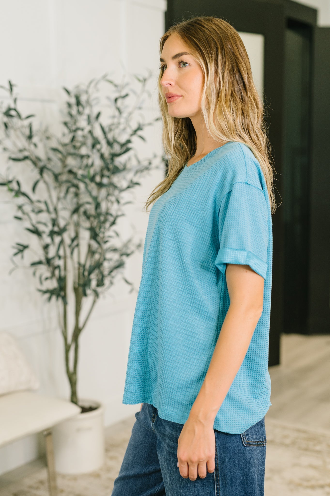 Woman wearing relaxed teal waffle knit tee with rolled sleeves paired with casual blue jeans in bright indoor space