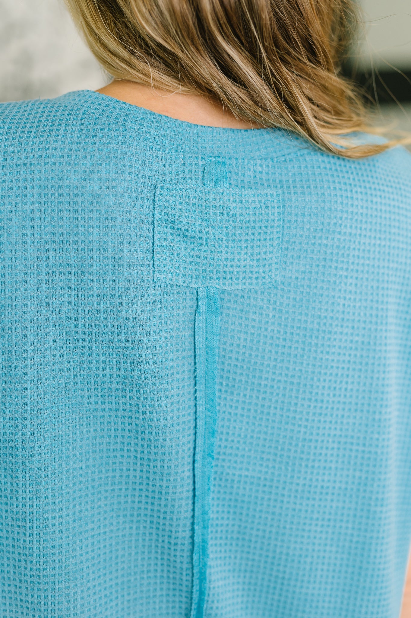 Close-up of teal waffle knit fabric textured with stitched seam detail on relaxed knit top back