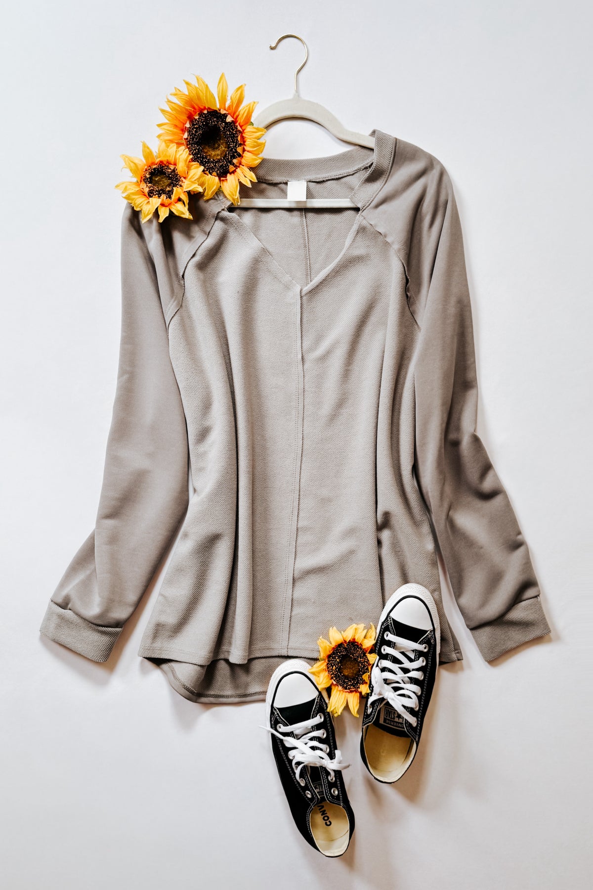 Beige textured knit top with a notched V neckline and raglan sleeves styled with sunflowers and black high top sneakers