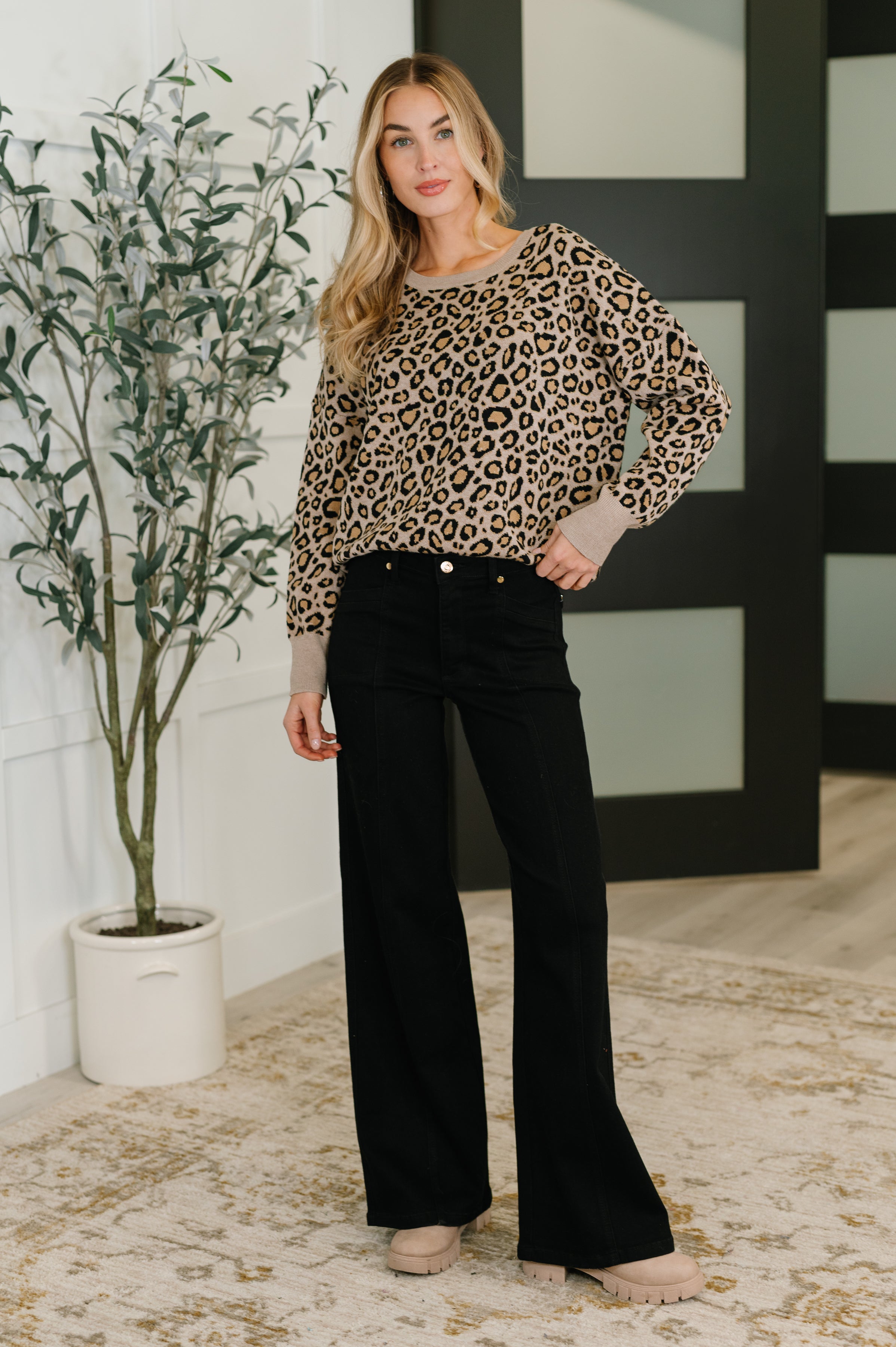 Woman standing indoors wearing a brown leopard print pullover with beige cuffs paired with black wide-leg pants