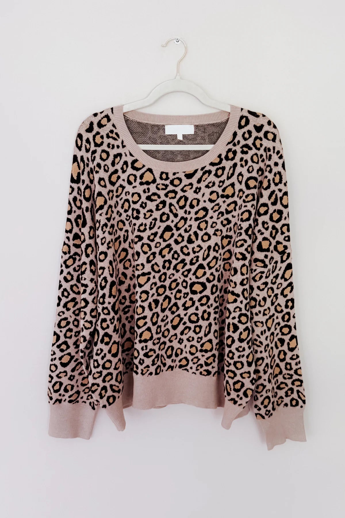 Brown leopard print long sleeve sweater with rounded neckline hanging on white hanger against plain wall