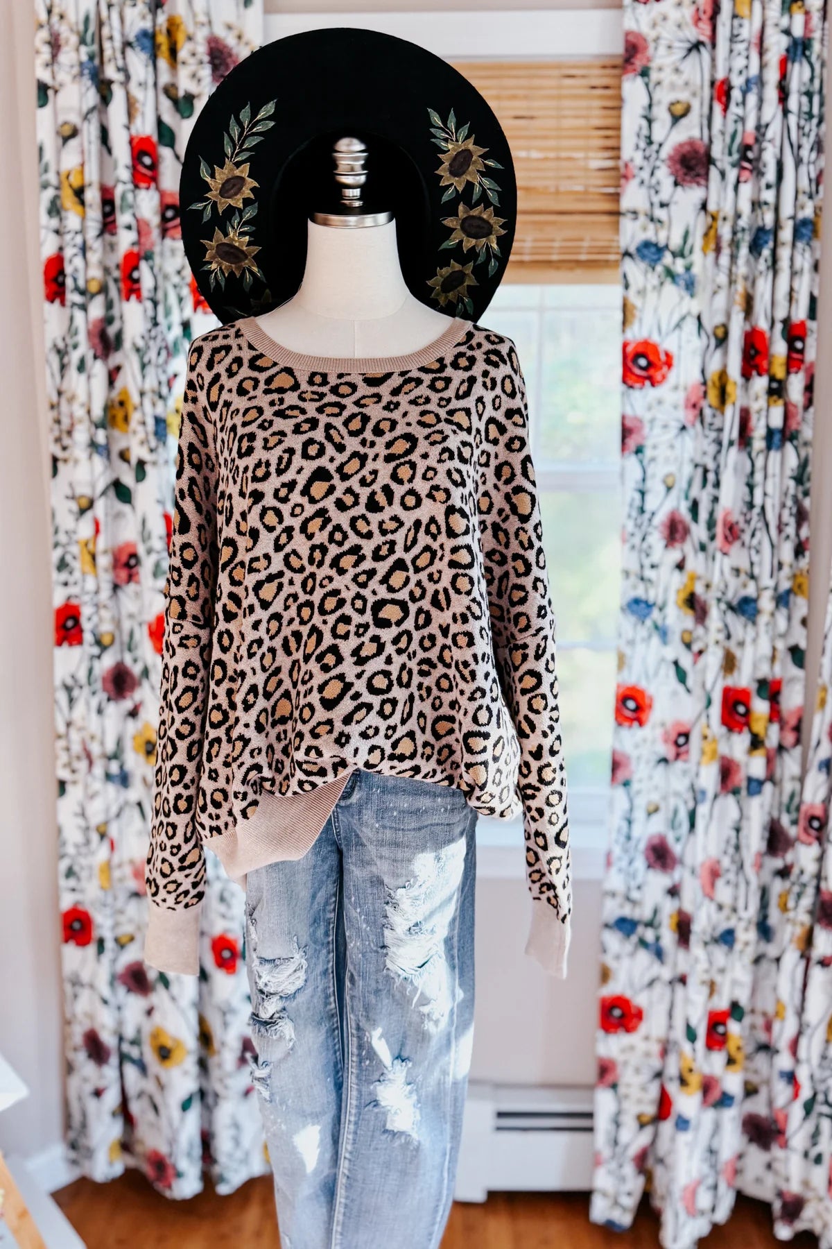 Brown leopard print sweater displayed on mannequin with distressed light wash jeans and black embroidered hat indoors