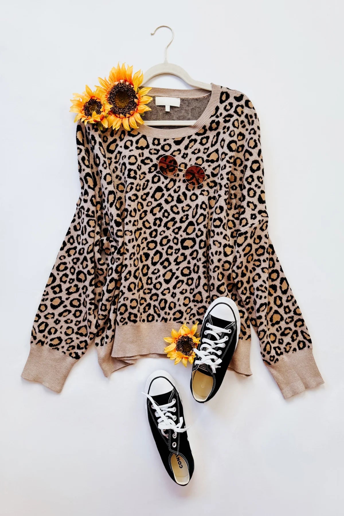 Brown leopard print sweater with long sleeves styled with black canvas shoes and sunglasses on a white background