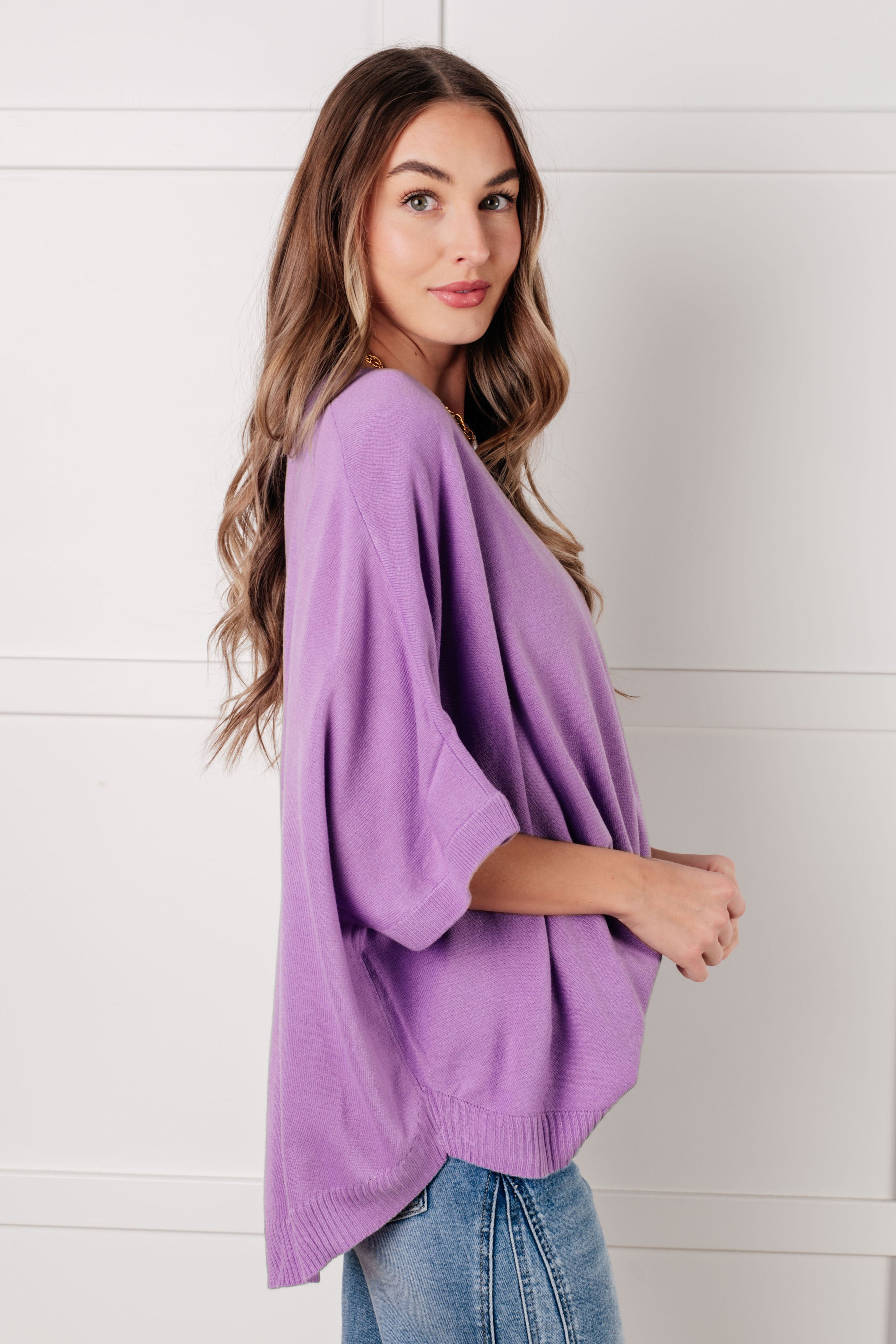 Woman wearing a loose lilac knit top with dolman sleeves paired with light wash denim jeans indoors