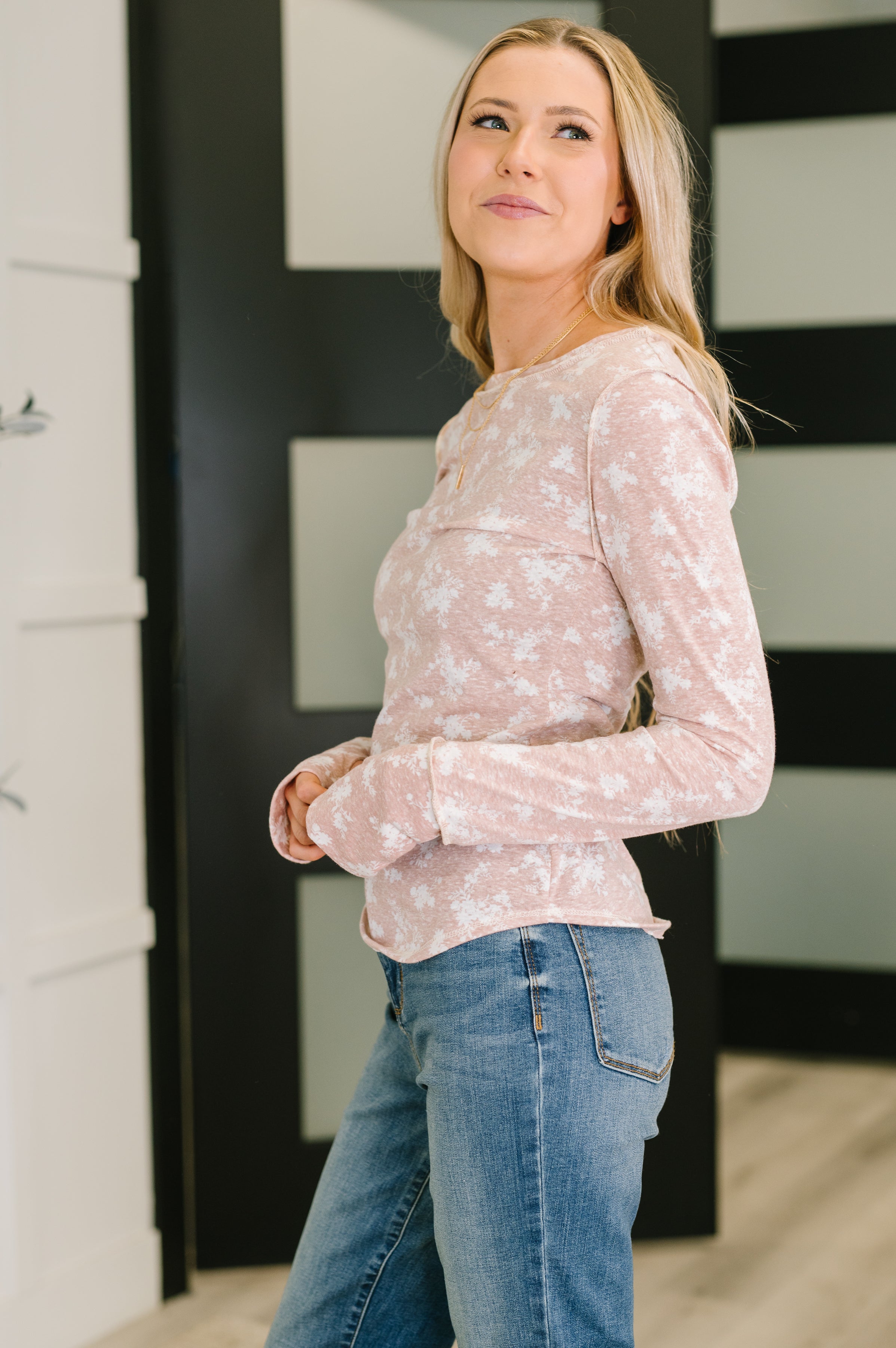 Woman wearing a fitted pink long-sleeve top with a subtle floral print paired with light blue jeans indoors
