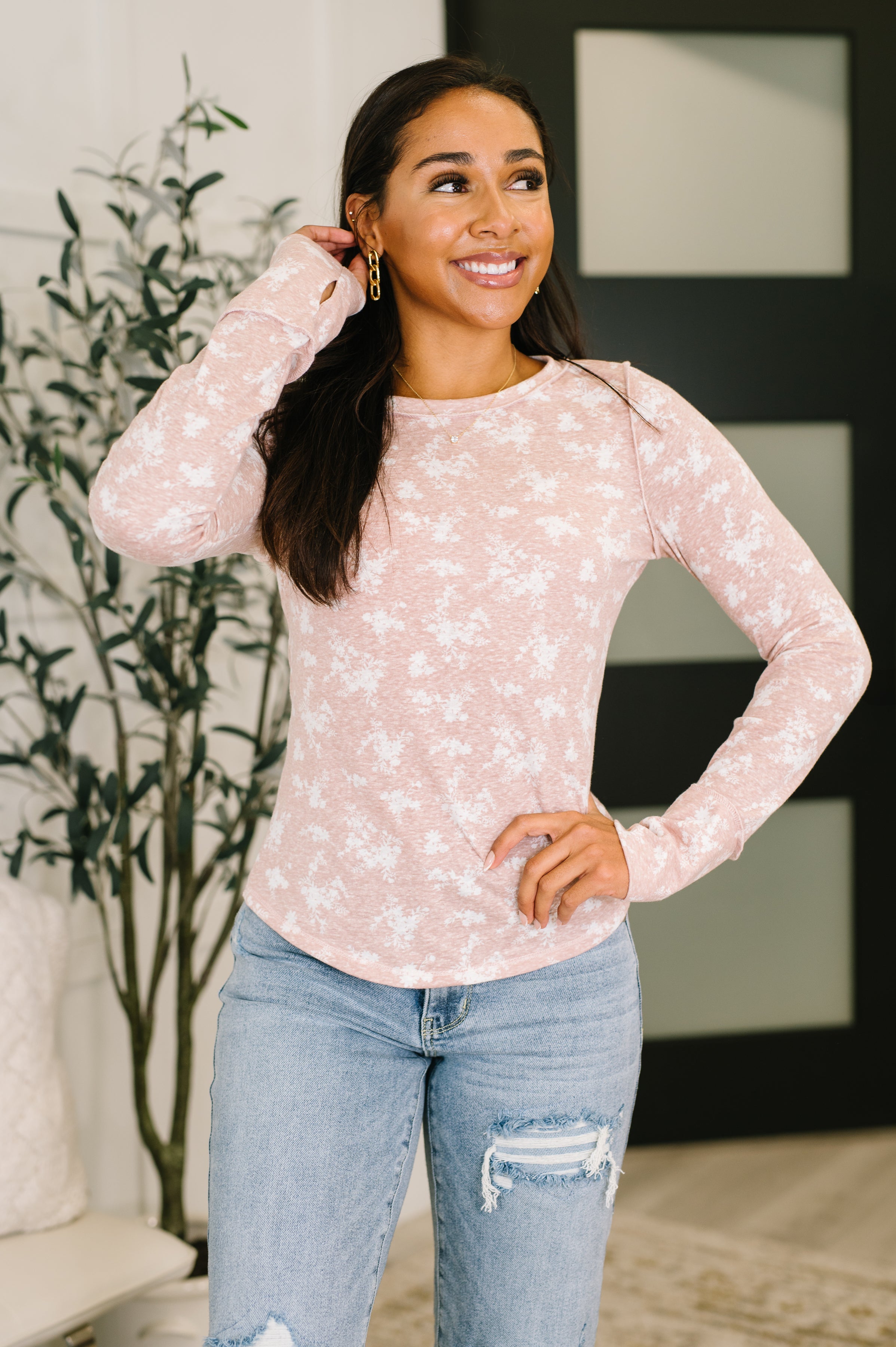 Woman wearing a mauve long sleeve top with white floral print and distressed blue jeans indoors