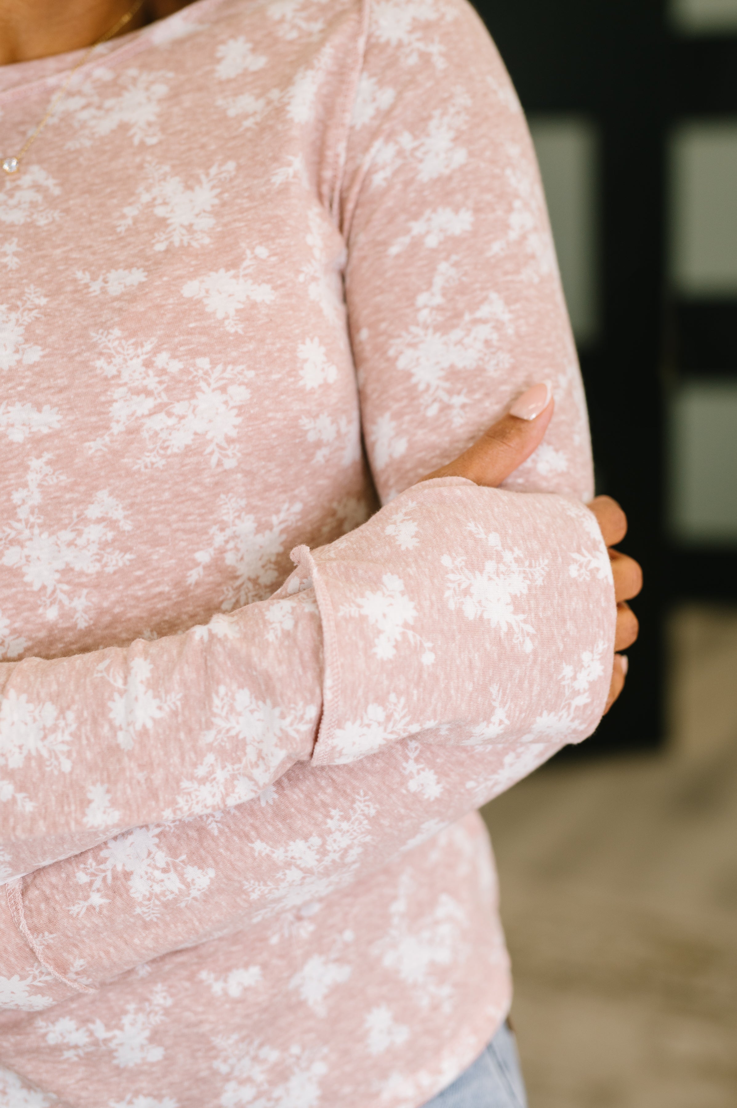 Close view of woman wearing a mauve long sleeve top with white floral print and extended cuffs indoors