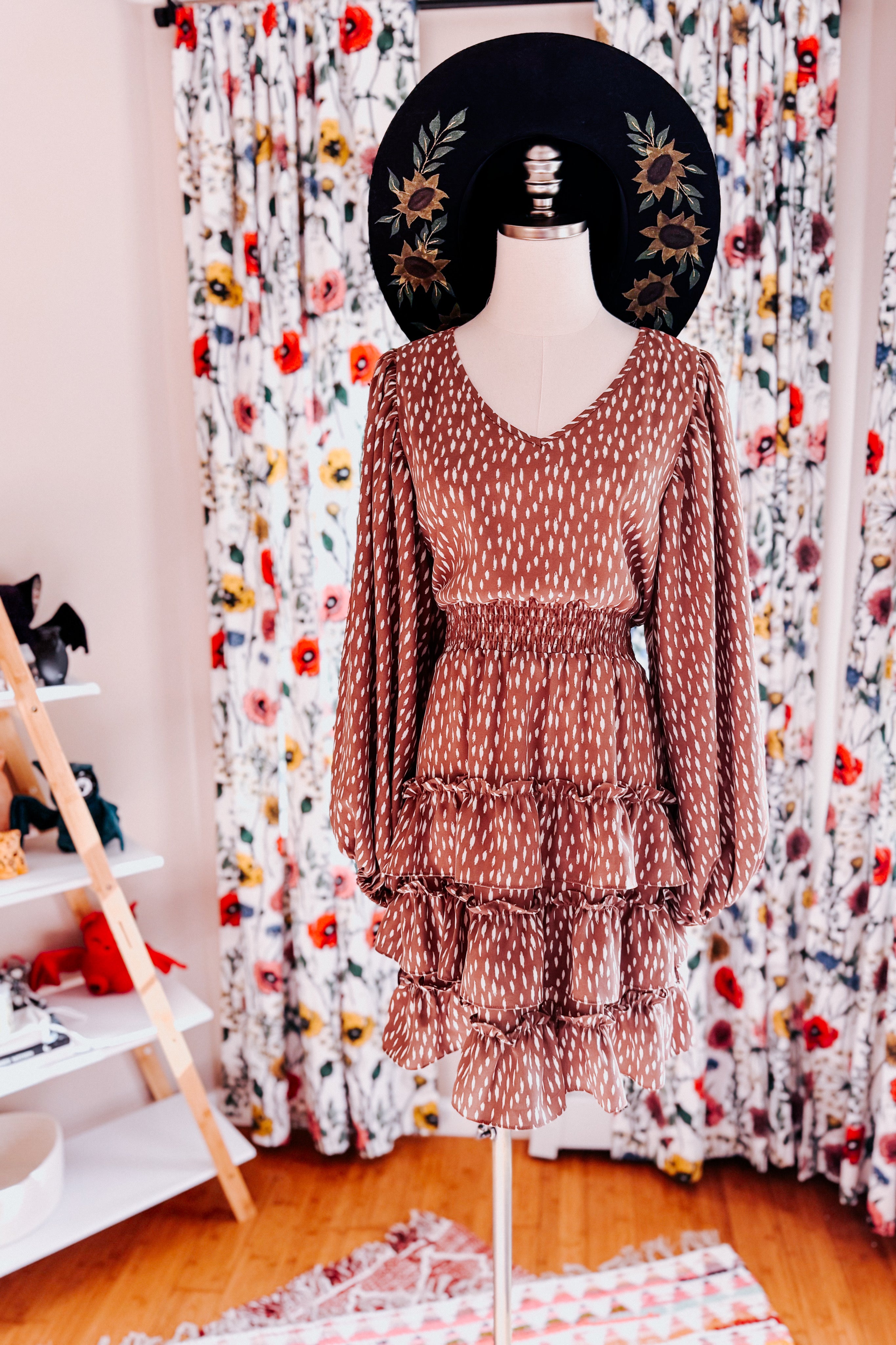 Terracotta dress with an abstract white dash pattern, gathered waist, long puffed sleeves, and tiered ruffled skirt on mannequin
