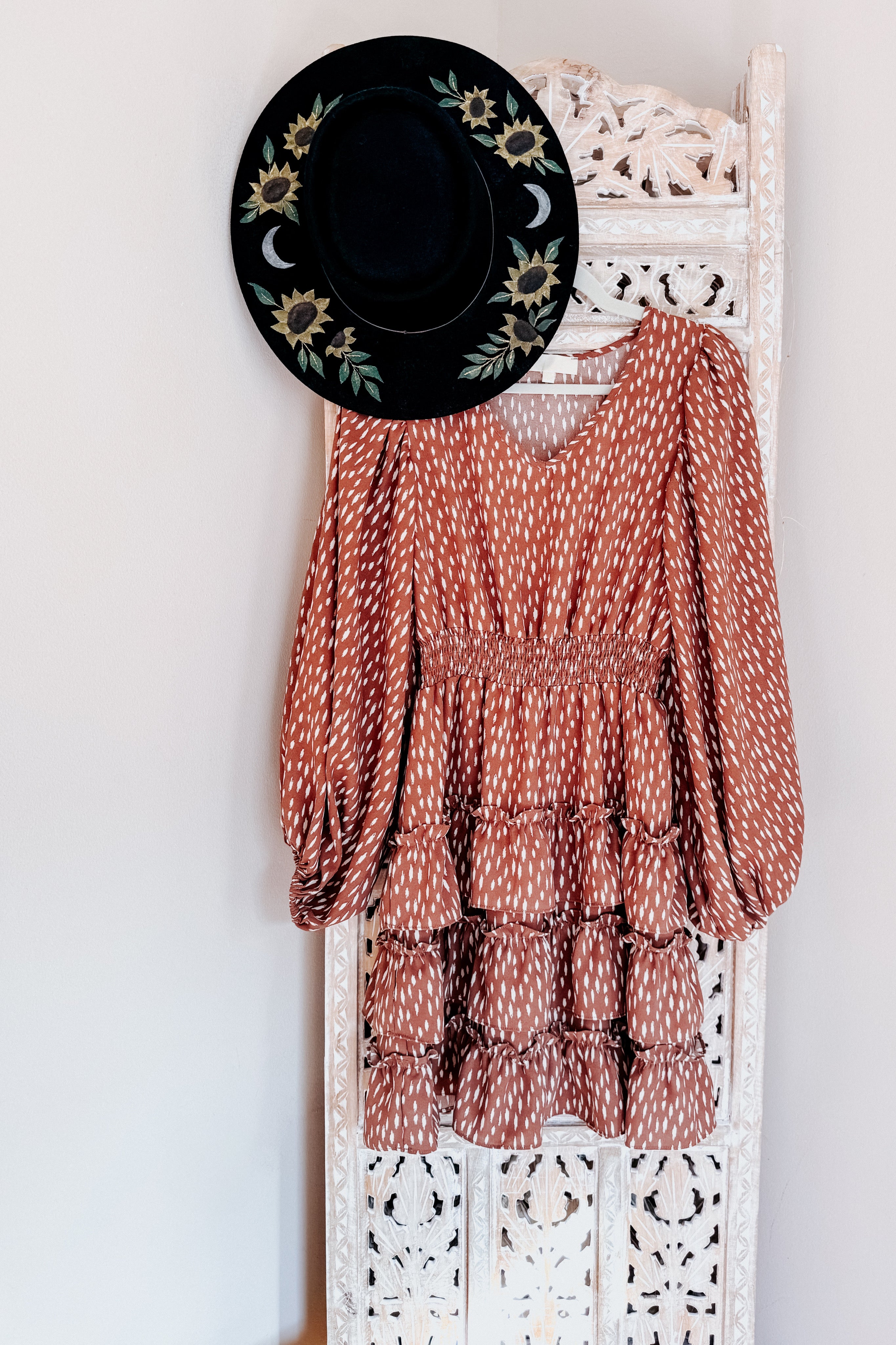 Terracotta dress with white dash pattern, elastic smocked waist, voluminous long sleeves, and layered ruffled skirt hanging with floral black hat